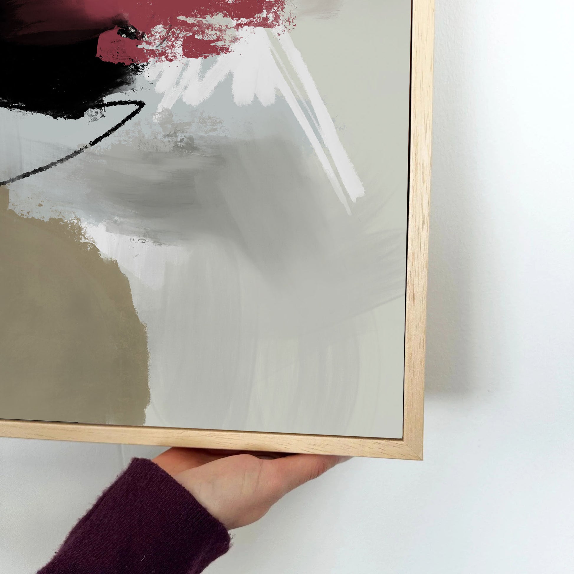 Hand holding a framed abstract painting on a white wall.
