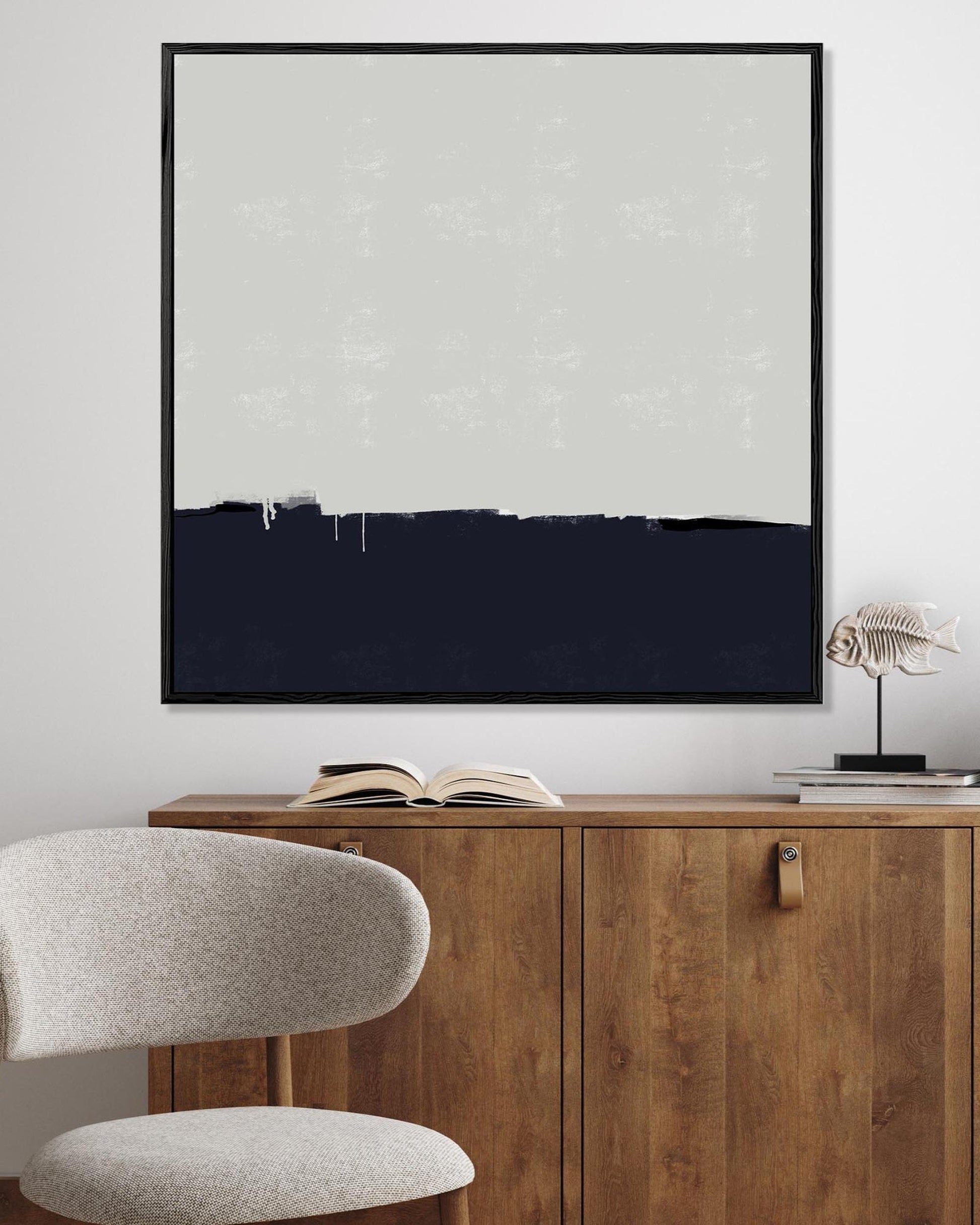 Framed artwork on a wall above a wooden cabinet with an open book and decorative items.