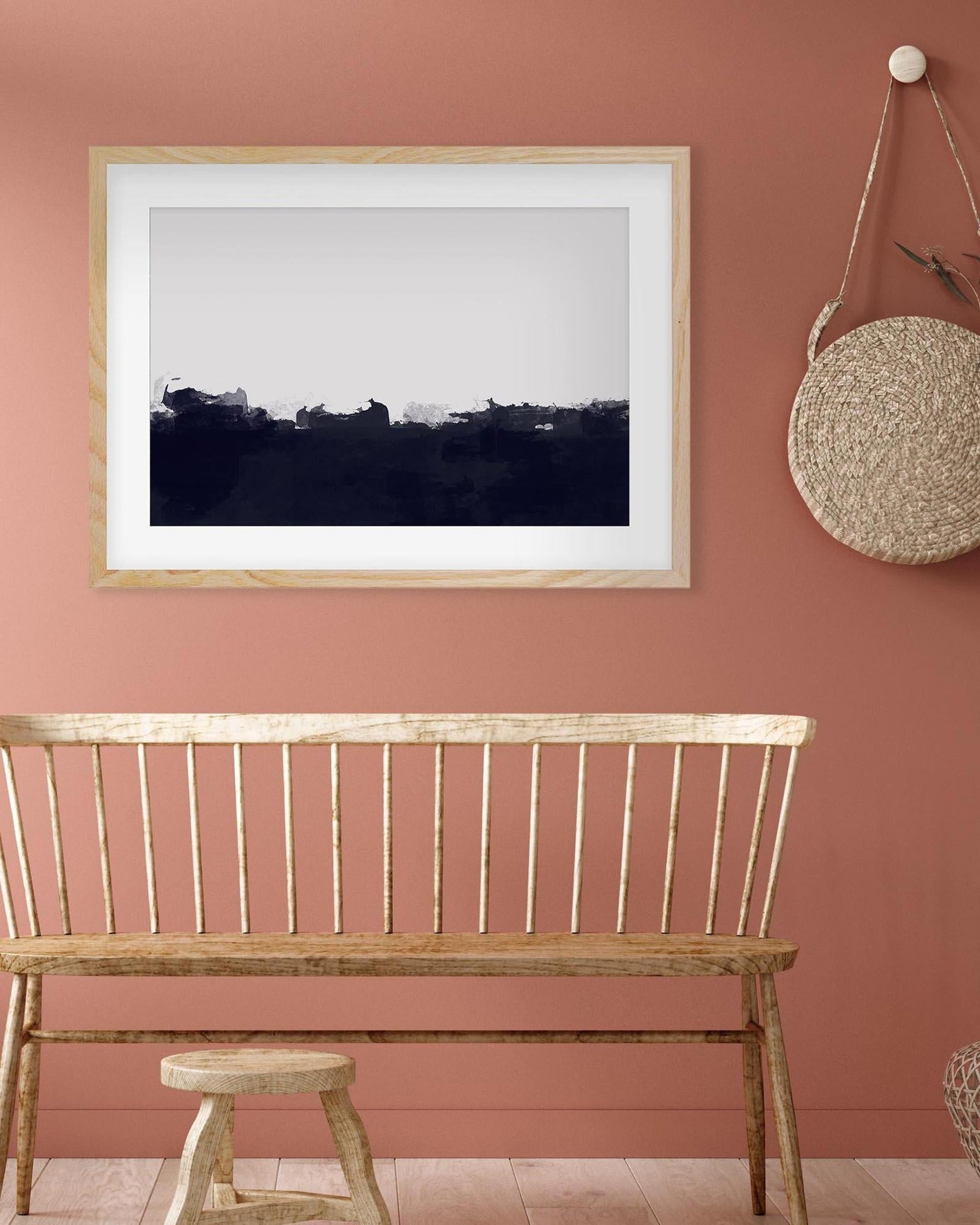 Wooden bench and stool against a pink wall with a framed black and white landscape print.