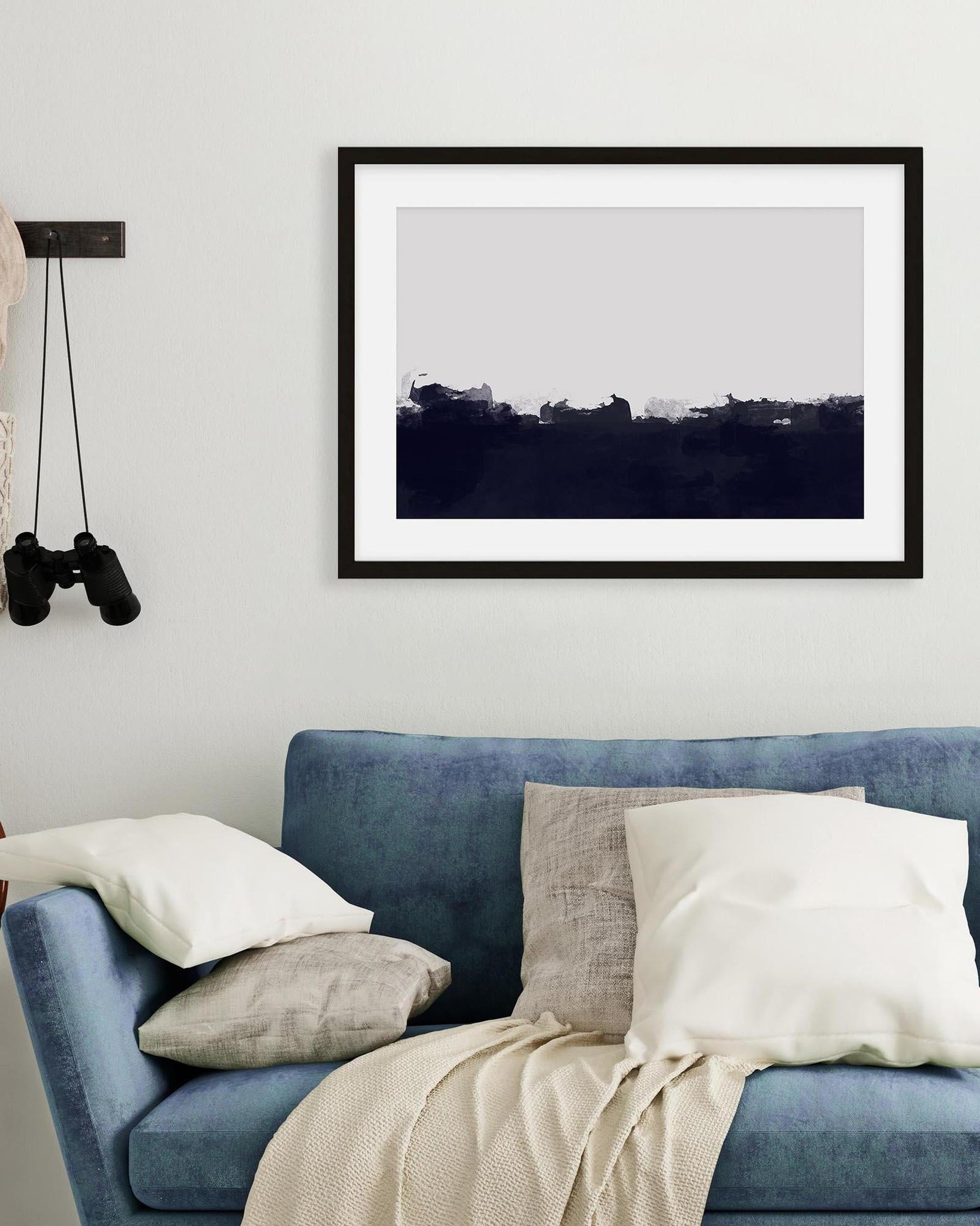 Framed artwork above a blue sofa with cushions and a blanket.