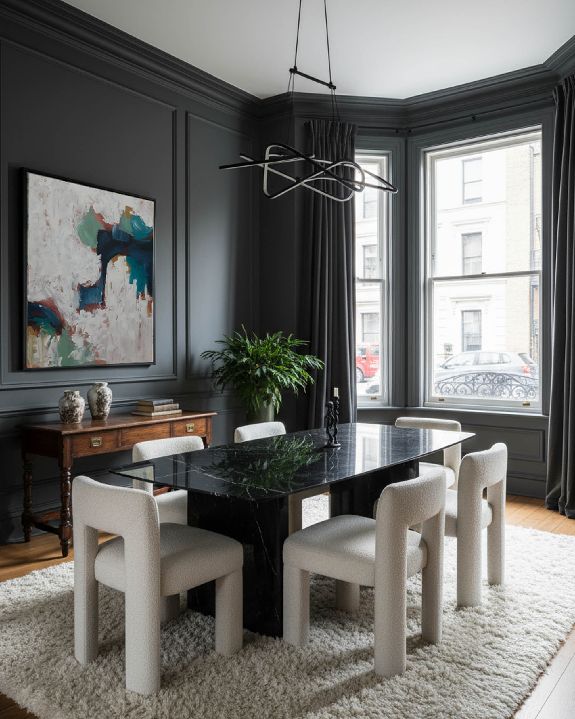 Modern dining room with dark marble table and white chairs, large windows, and abstract art on the wall.