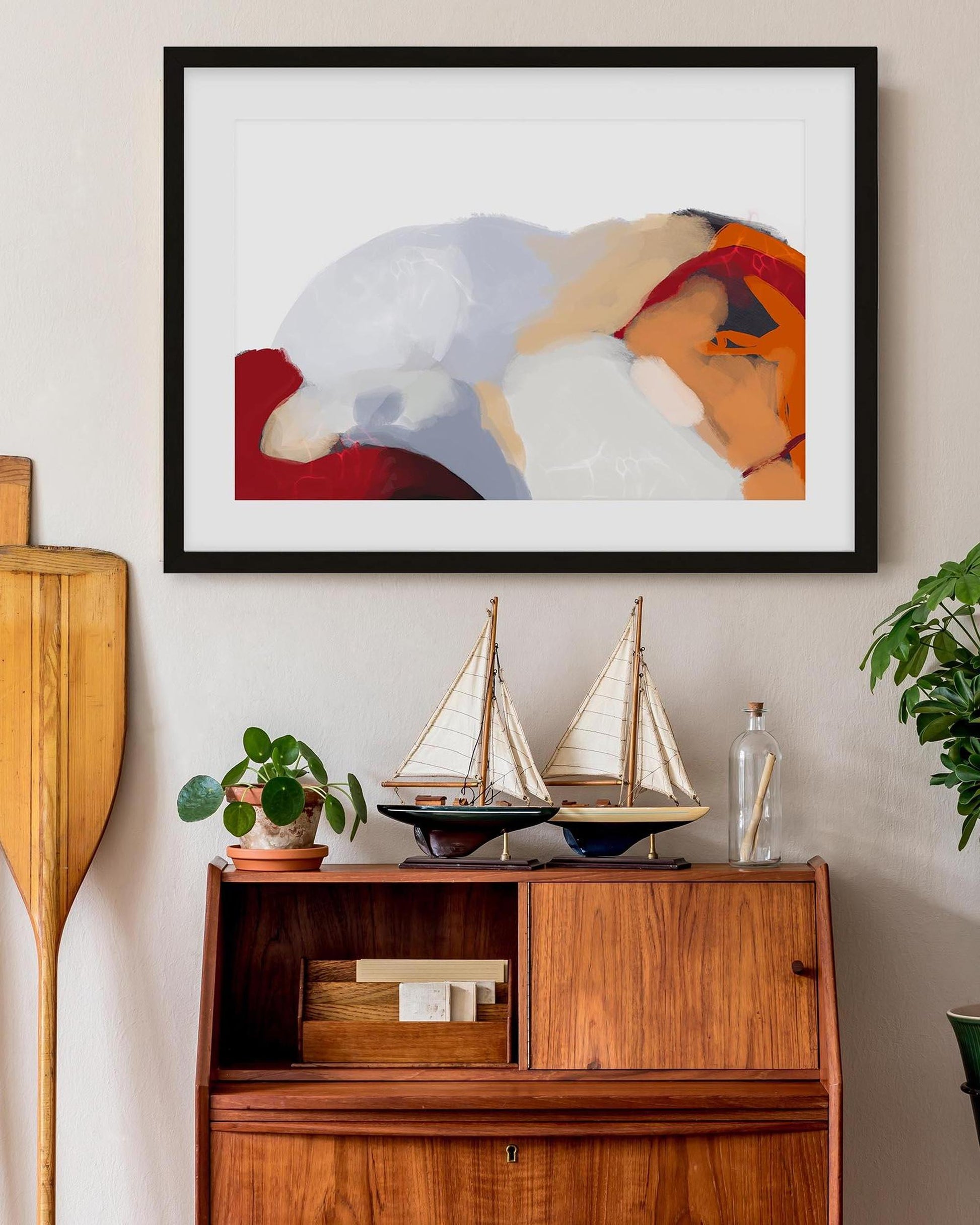 Framed abstract art above a wooden cabinet with decorative items