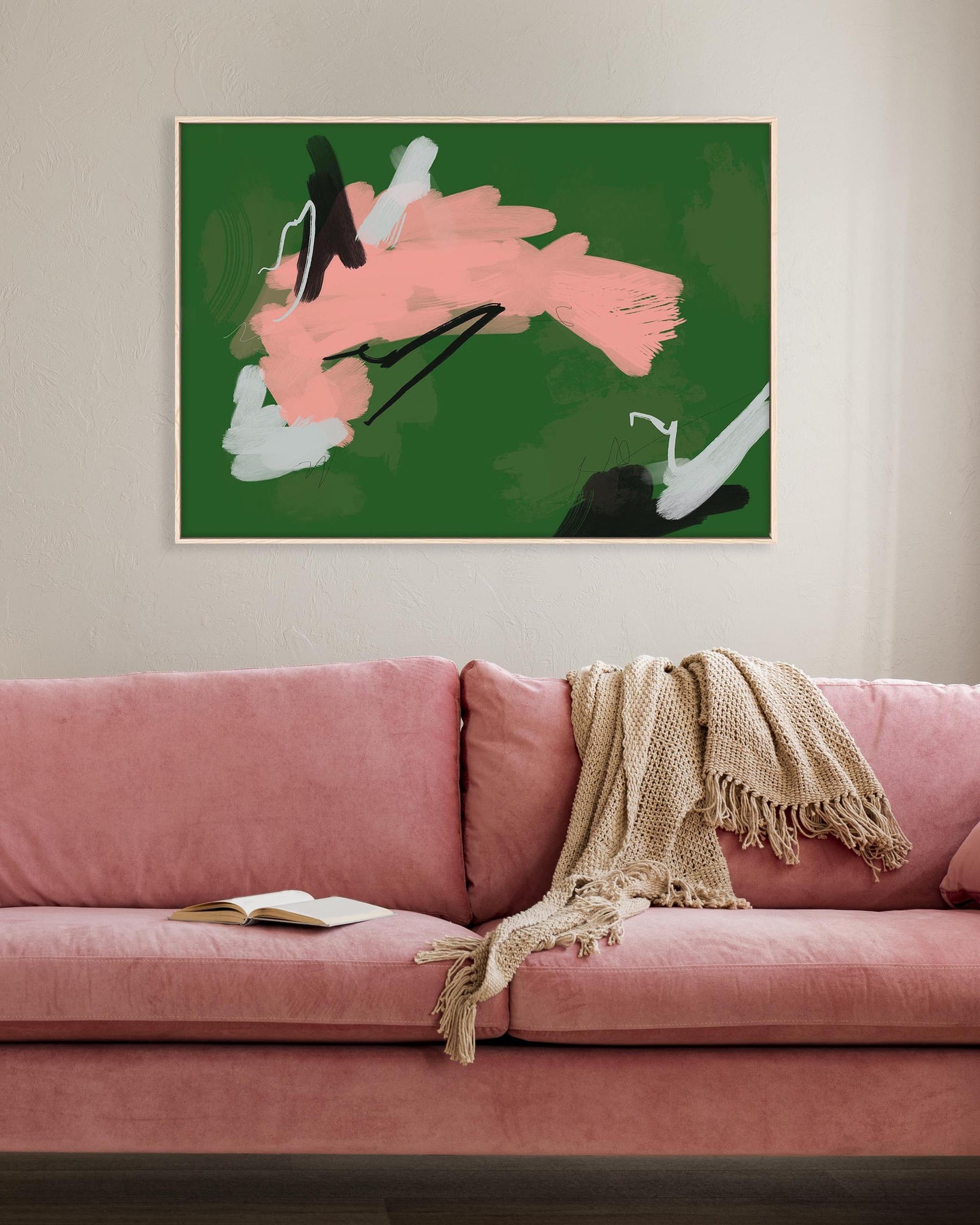 Pink sofa with a blanket and book in a room with abstract art on the wall.