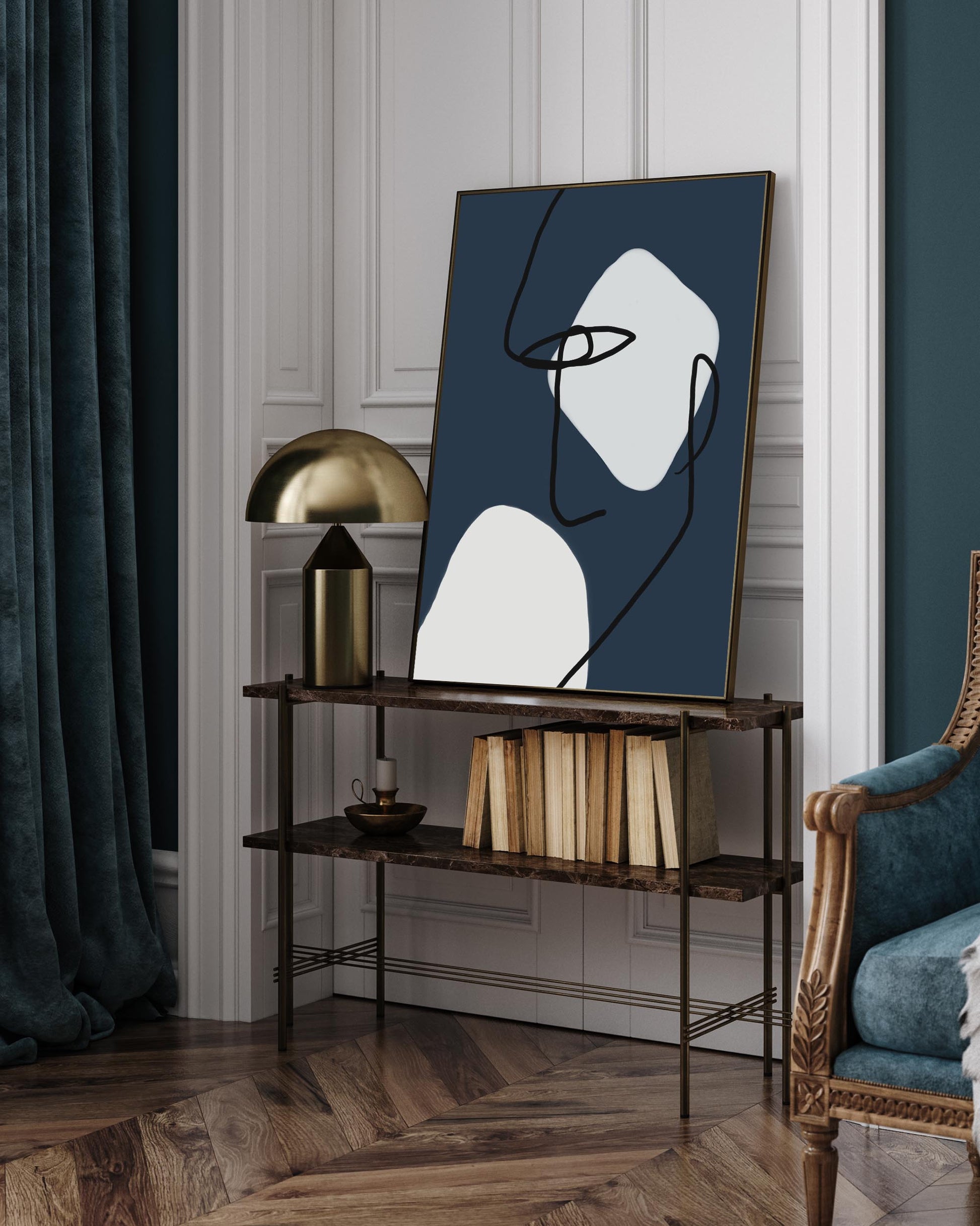 A navy and blue line drawing on canvas, framed and displayed above a console table in a room with dark curtains and a gold lamp.