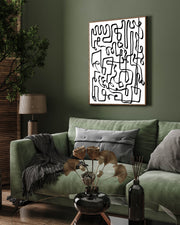 A framed canvas with a black, curved line abstract design hanging on a green wall above a sofa with cushions, with a plant and a lamp in the room.