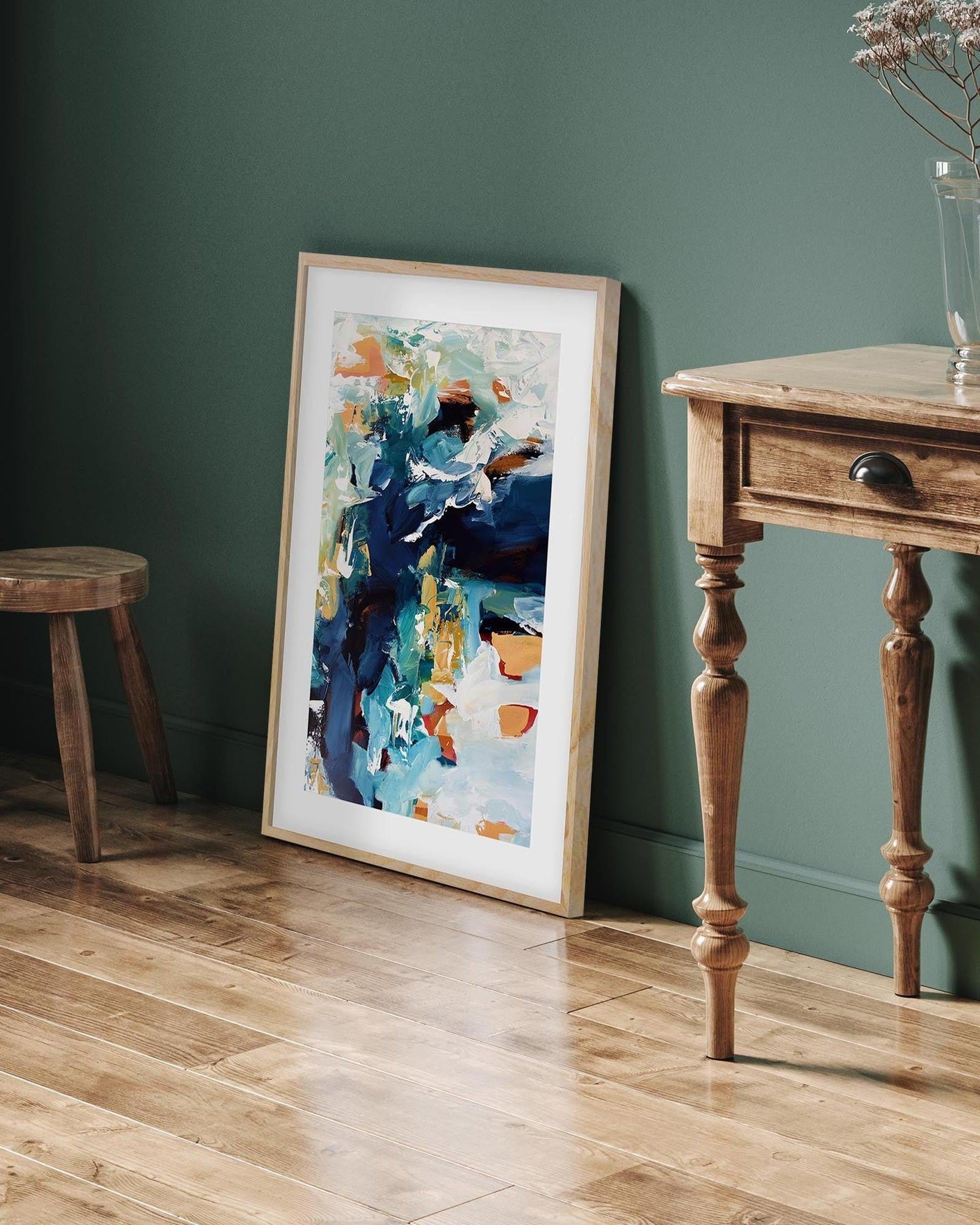 framed abstract poster in oak frame leaned on a green wall