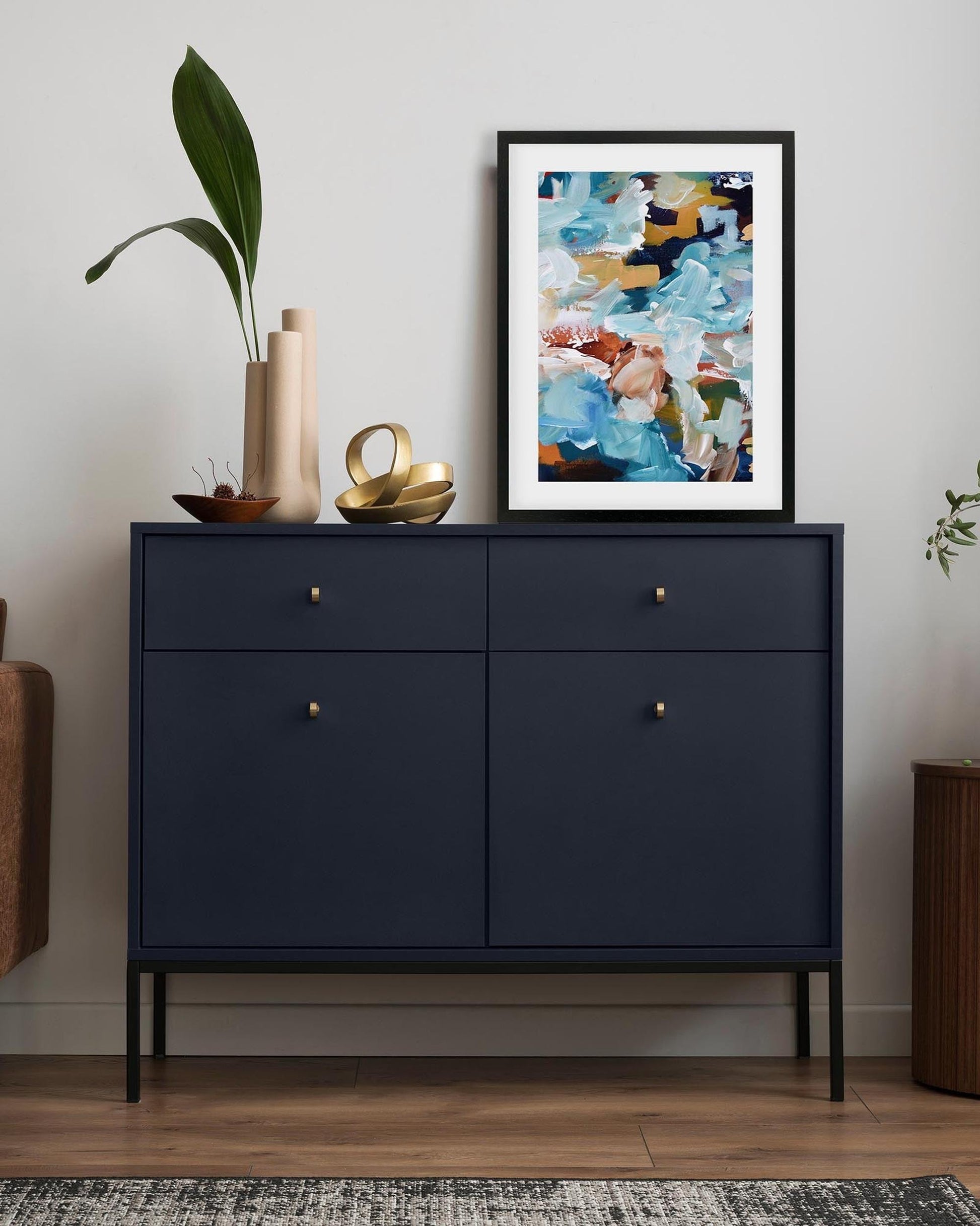 Navy blue dresser with decorative items and a colorful abstract painting in a living room setting.