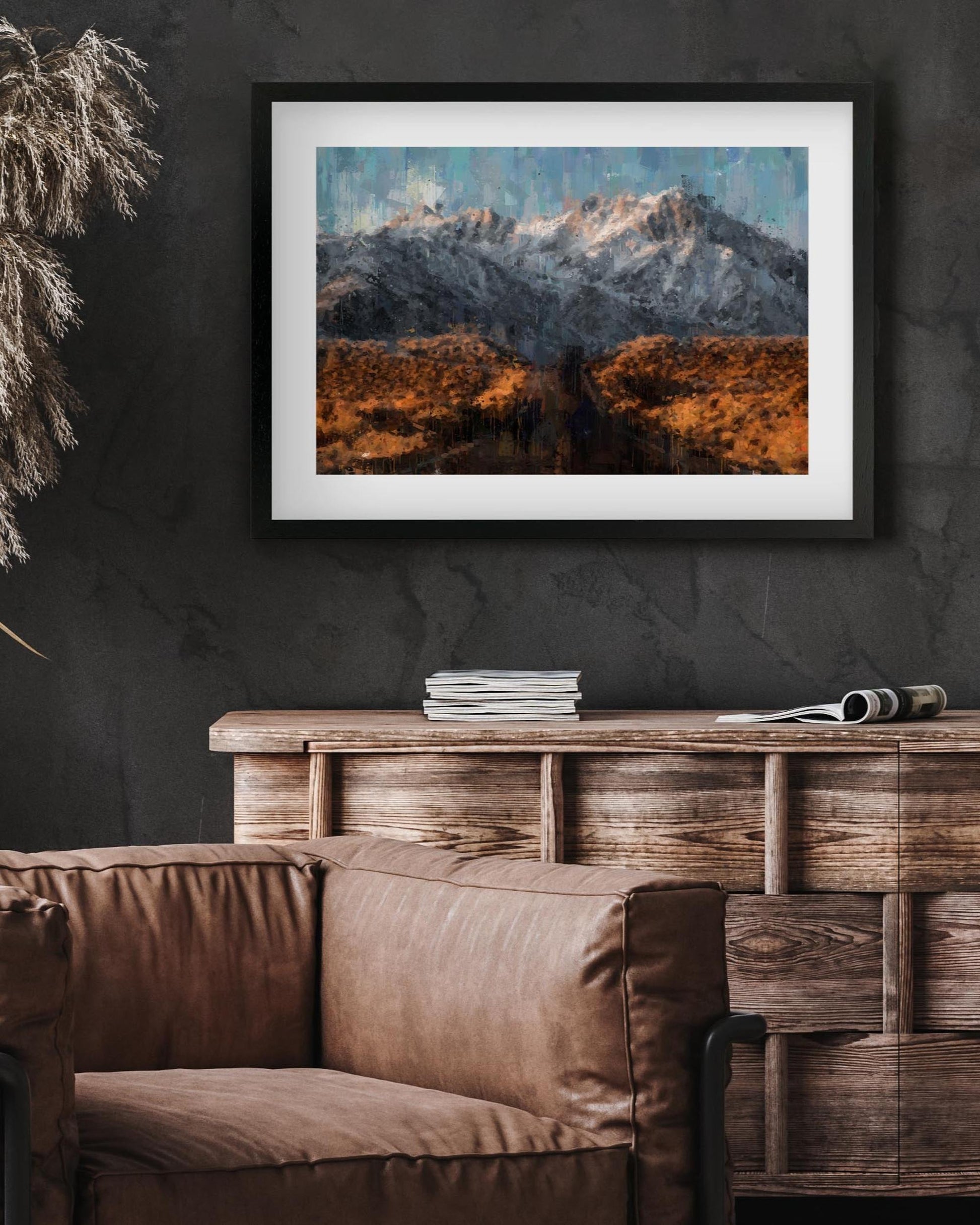 Framed mountain landscape print on a dark wall above a wooden console table with a brown sofa.