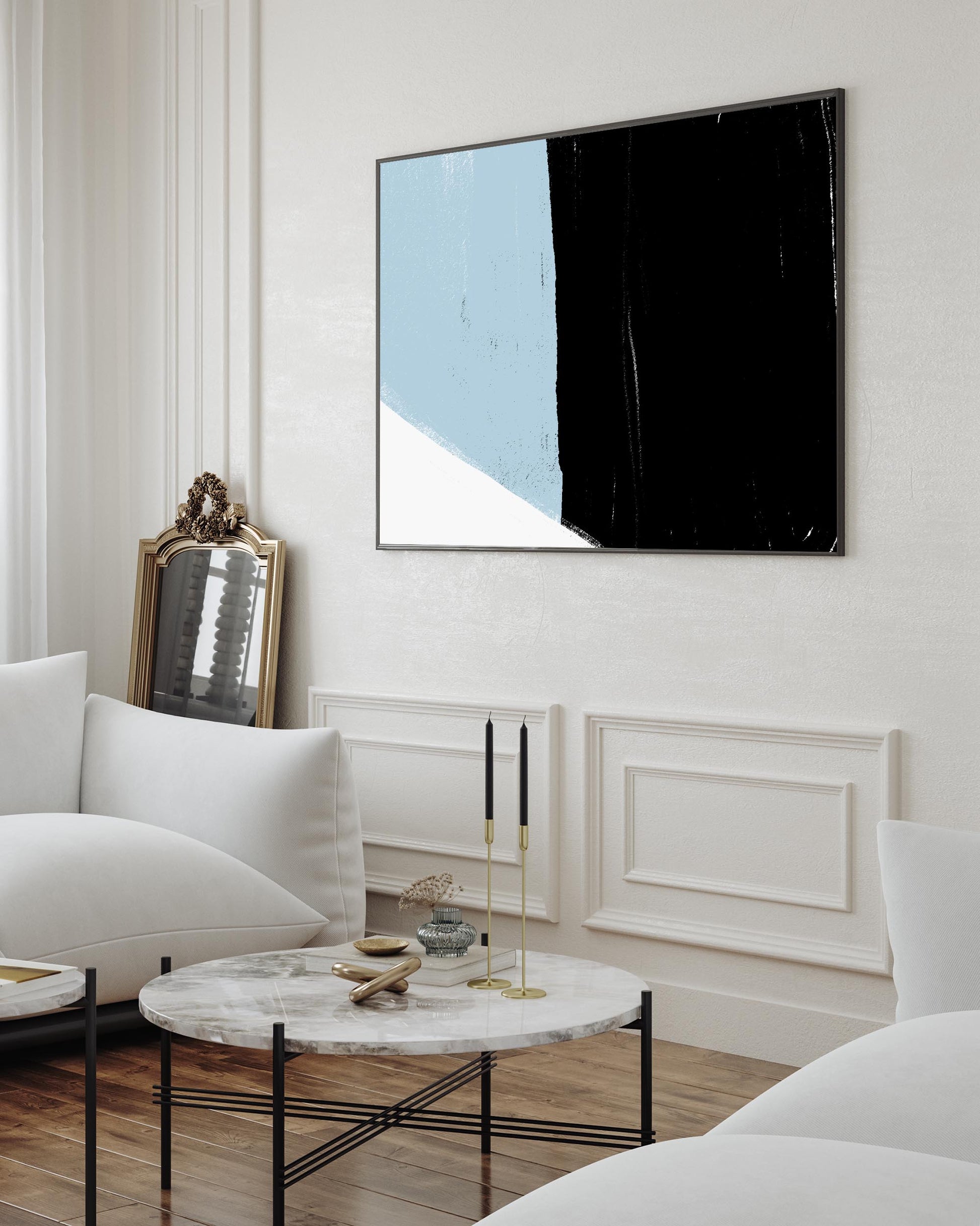 A framed canvas art print featuring bold abstract color blocks in black and blue, displayed above a white sofa in a bright living room setting.