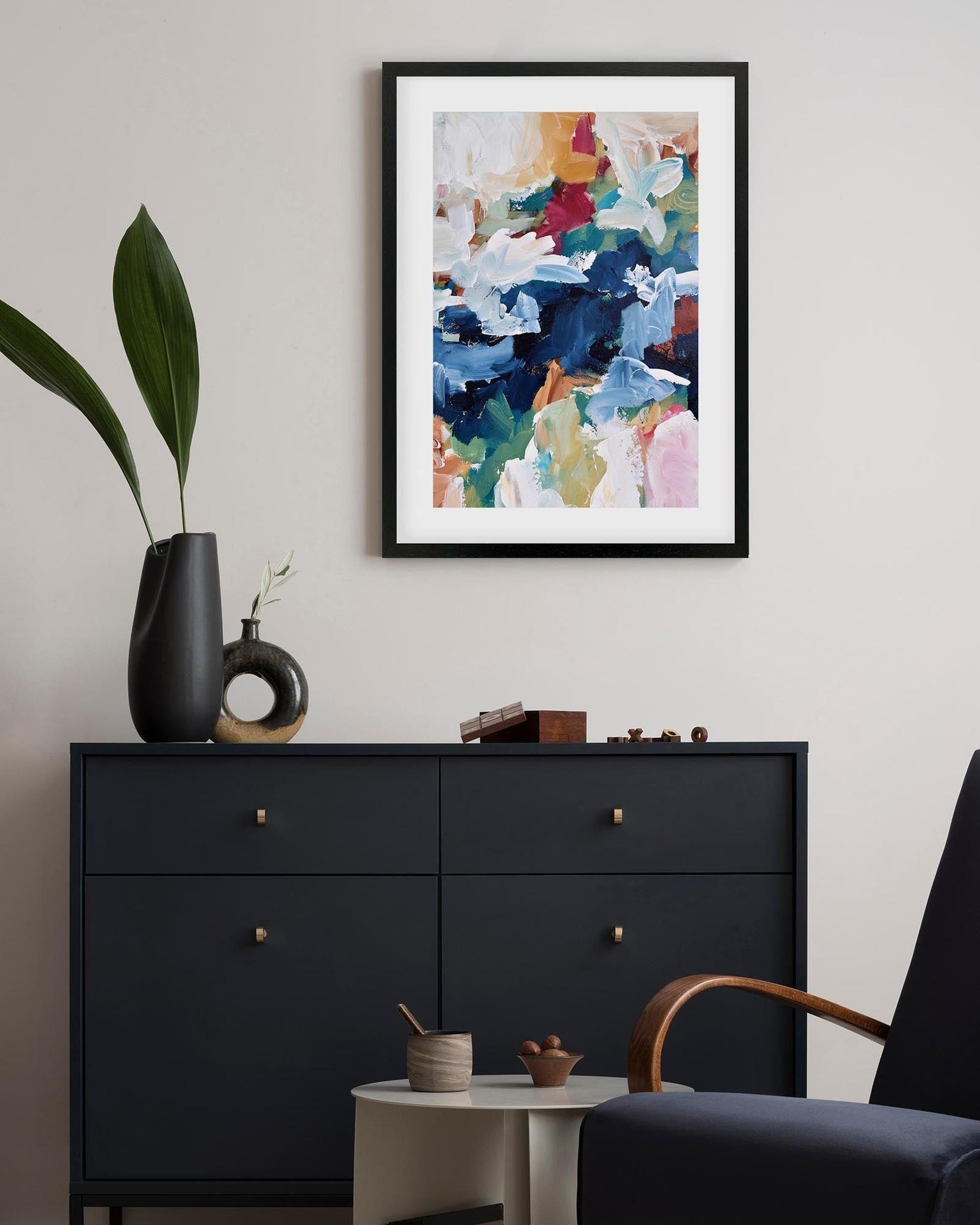 Framed abstract art above a black dresser with decorative items in a room.