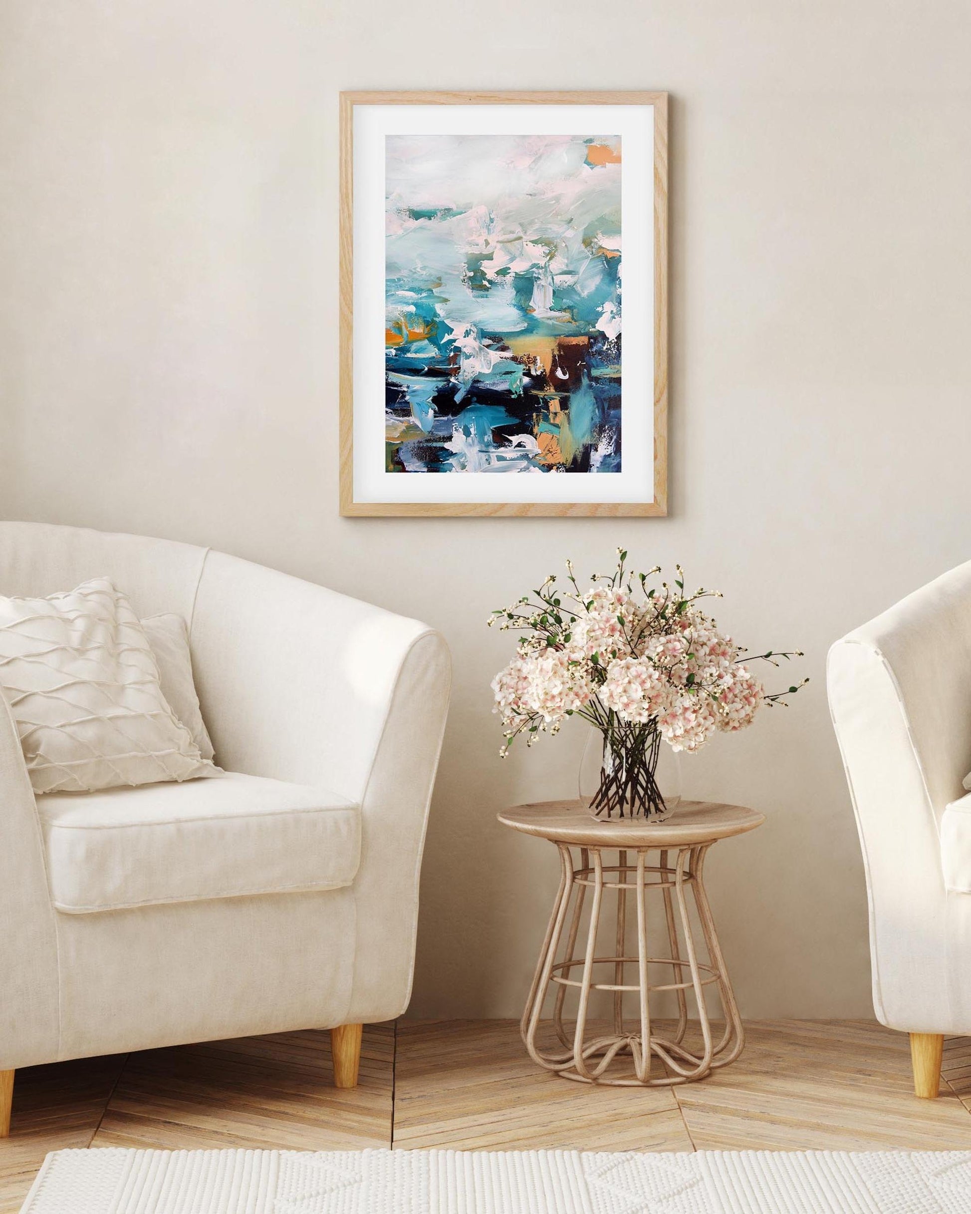 Living room with two white armchairs, a small table with flowers, and a colorful abstract painting on the wall.