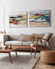Two beige abstract canvas art pieces mounted on a wall above a grey sofa and a wooden coffee table in a living room setting.