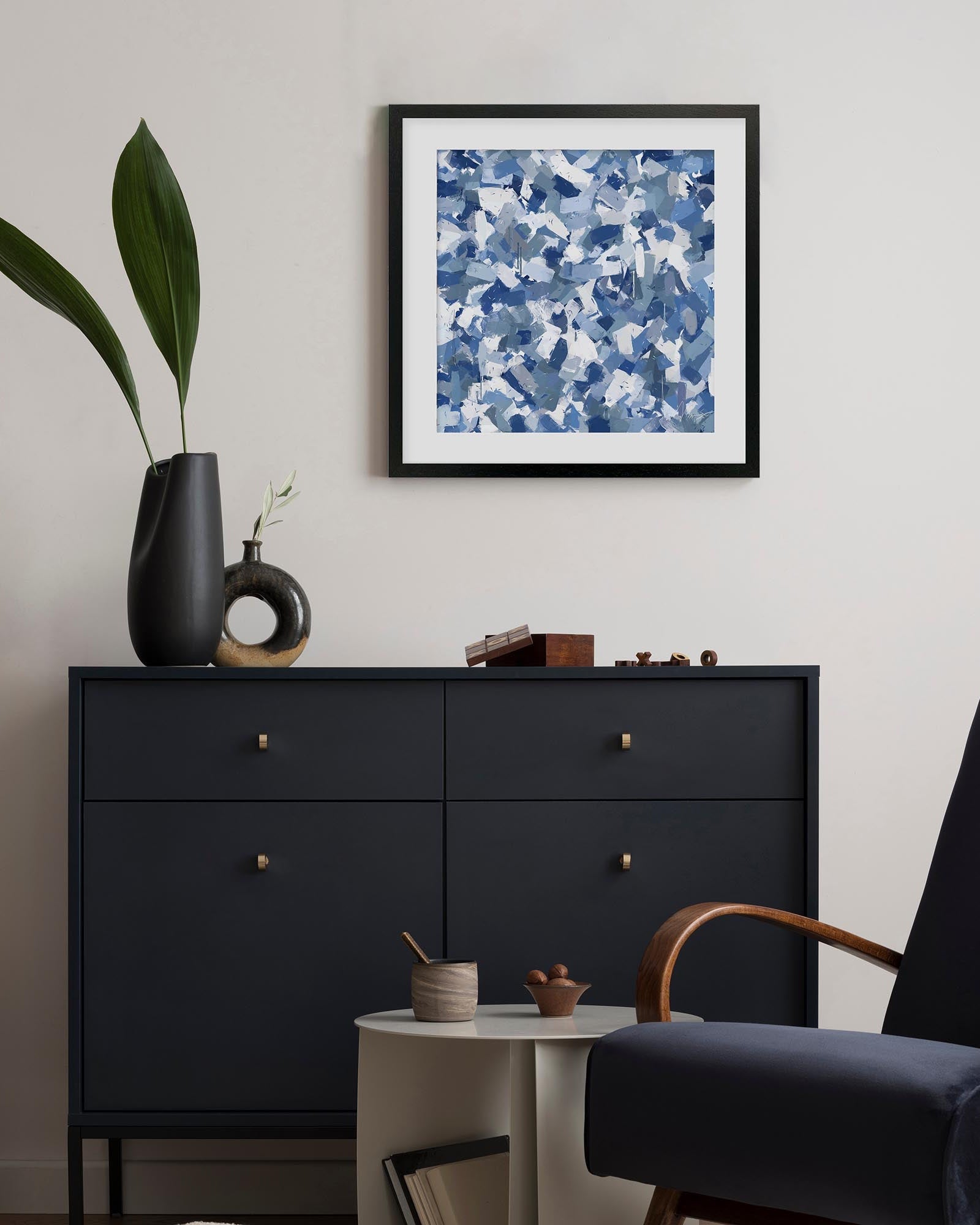 Framed blue abstract art piece on a wall above a black dresser with decorative items.
