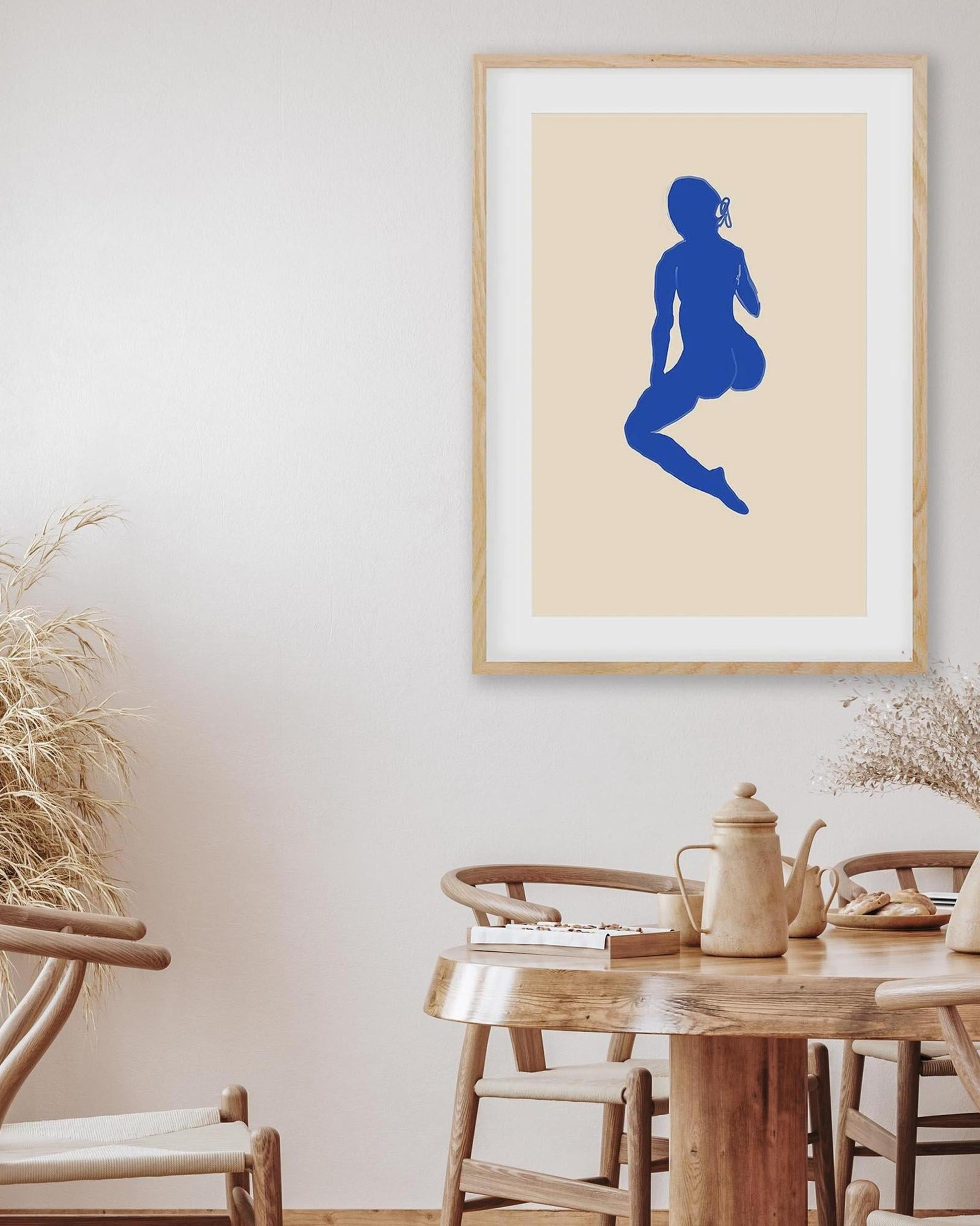 Framed artwork of a blue silhouette on a beige wall above a wooden dining table.