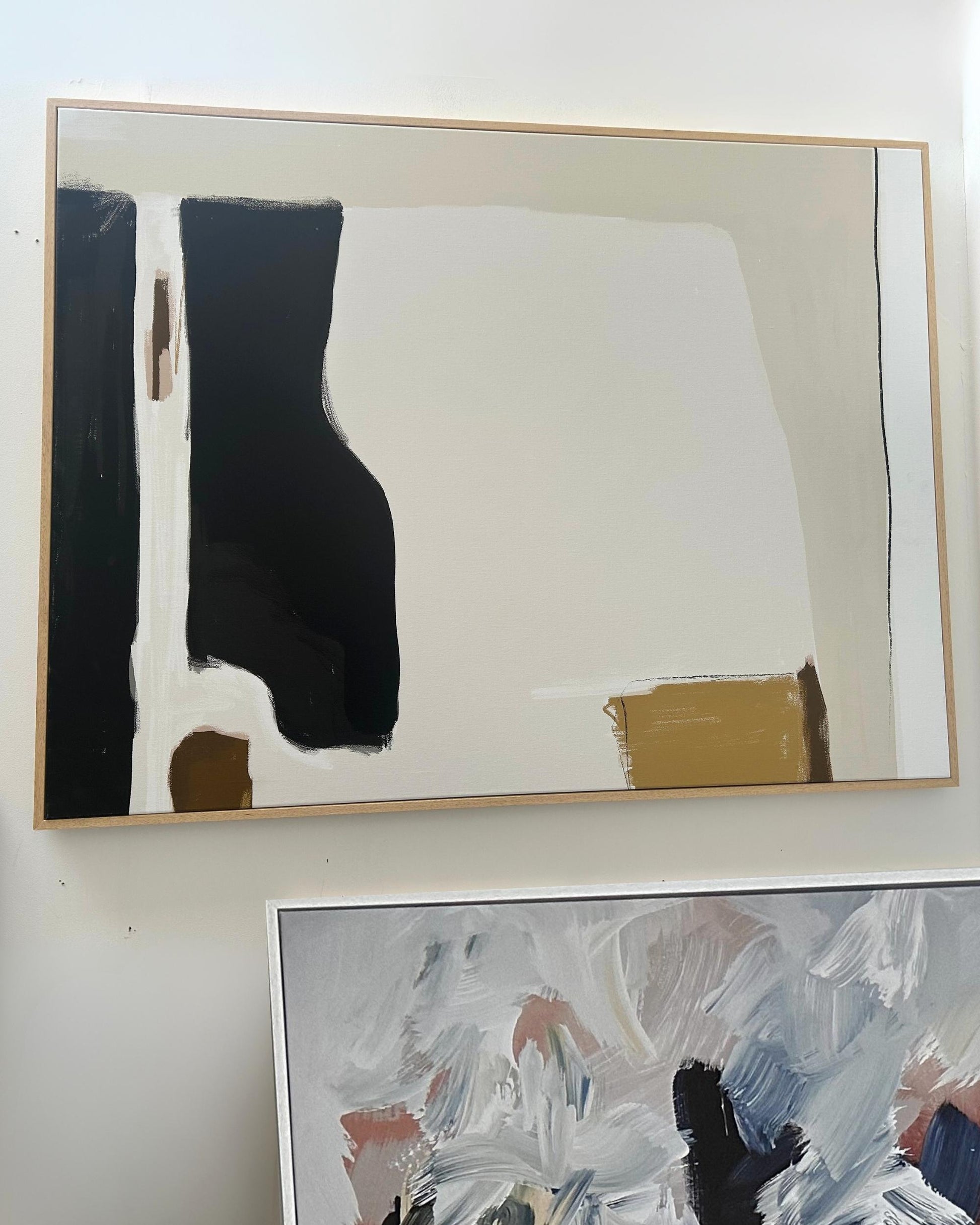 Abstract art piece with black, white, and gold colors on a white wall.