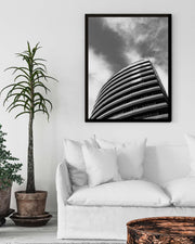 Framed black and white architectural print on a wall above a white sofa with decorative plants.