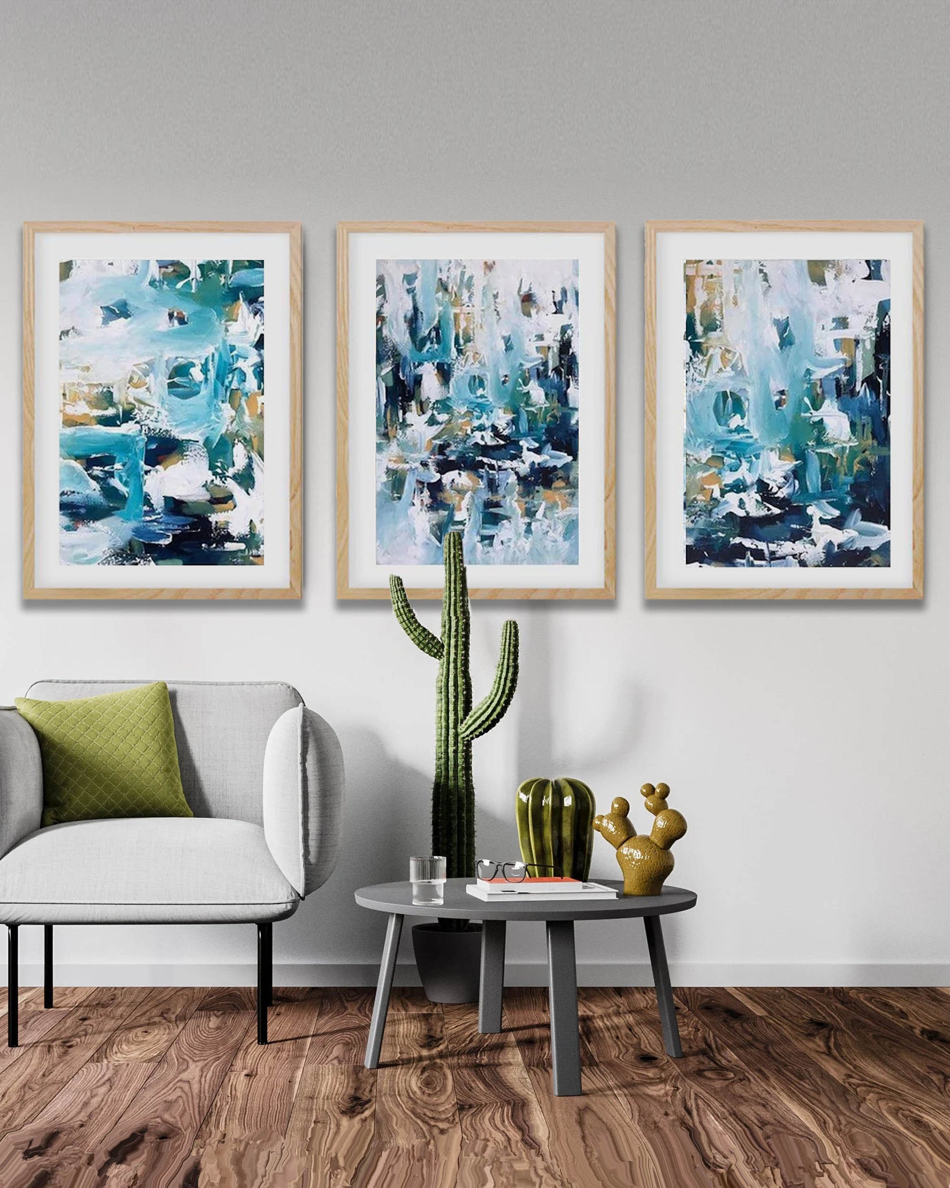 Three abstract art pieces on a wall above a gray sofa with a cactus plant.