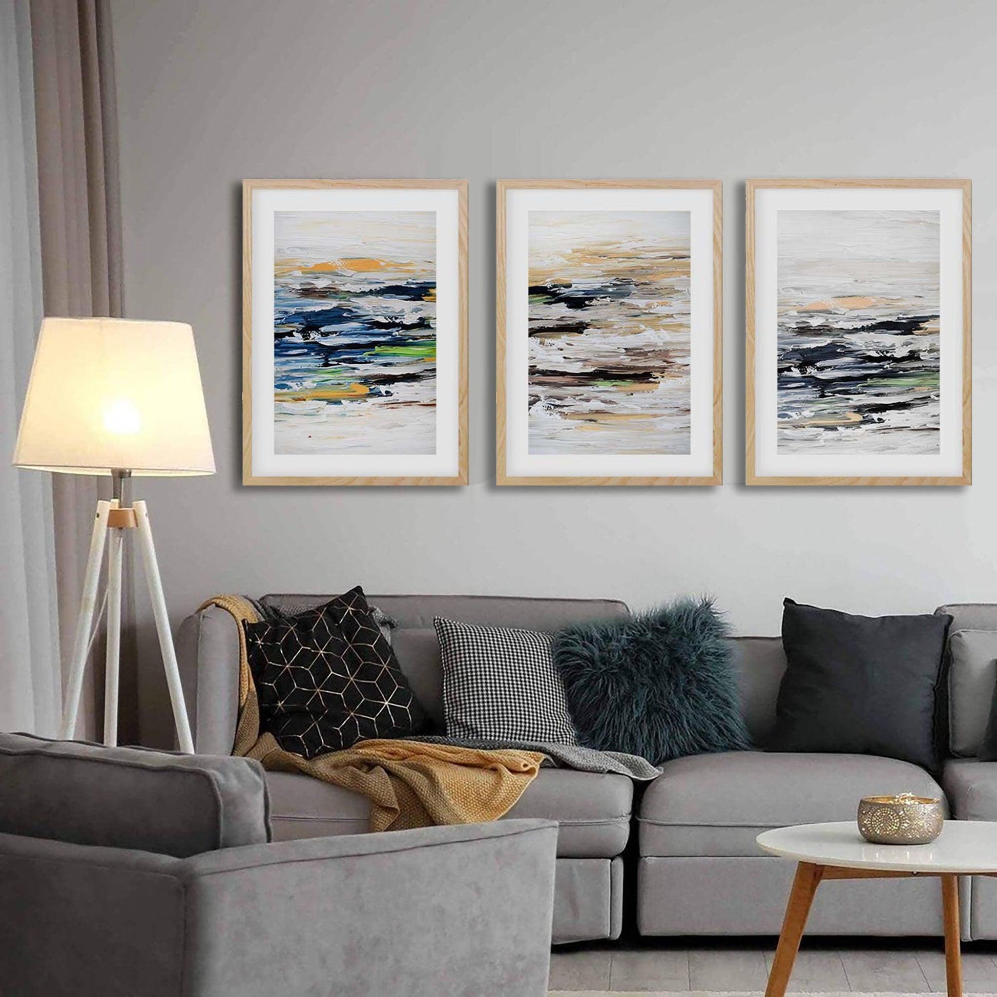 Modern large wall art prints set of 3, muted brown home decor, stylish luxury living room. Grey sofa with decorative pillows in a living room setting with abstract art on the wall.