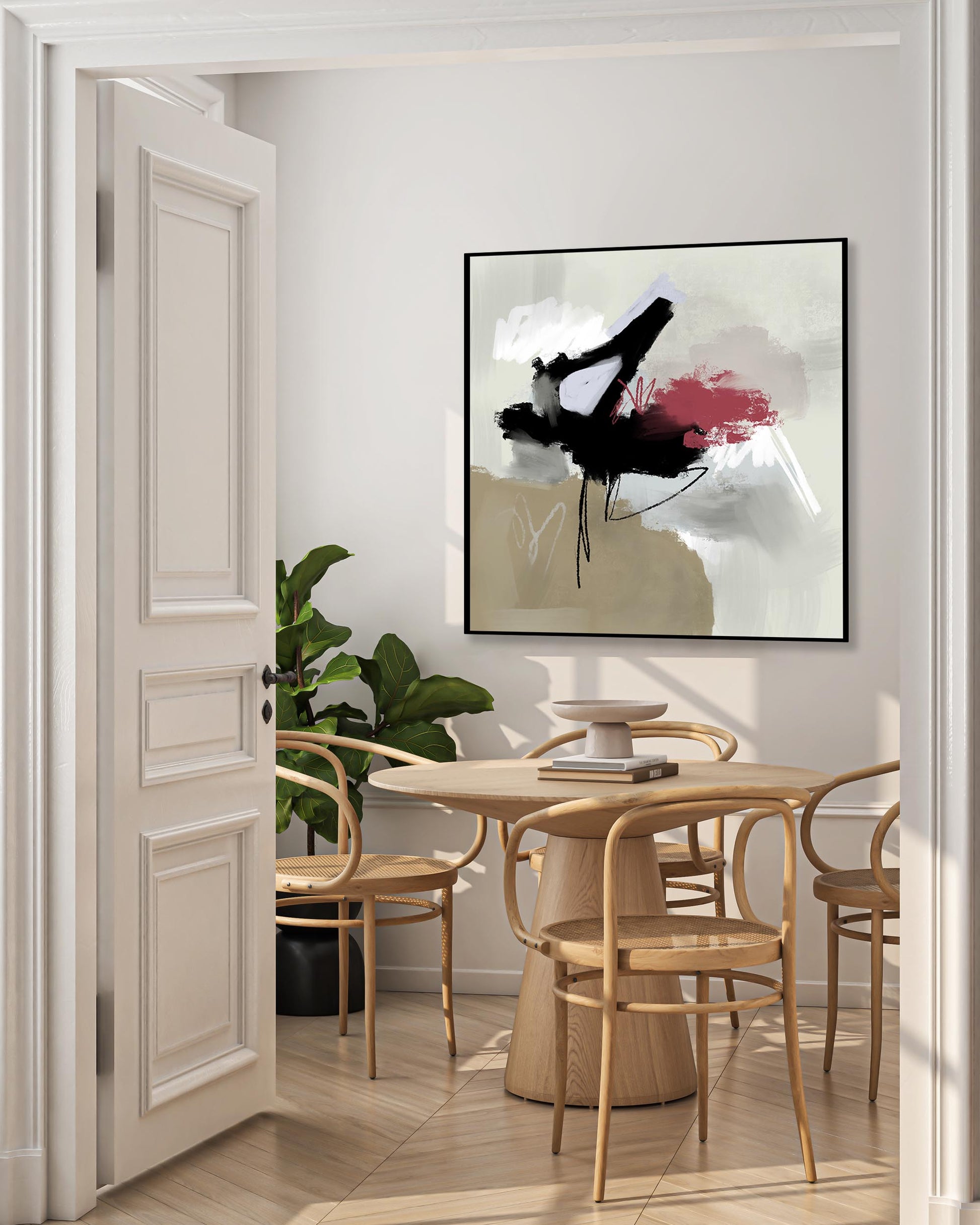 A large abstract framed canvas artwork featuring muted grey and soft beige-brown tones with splashes of black and raspberry, displayed in a well-lit room with a round dining table and chairs in the foreground.