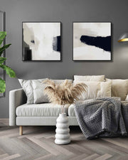 Large square monochrome black and white abstract art prints on canvas in stylish modern living room displayed above sofa.