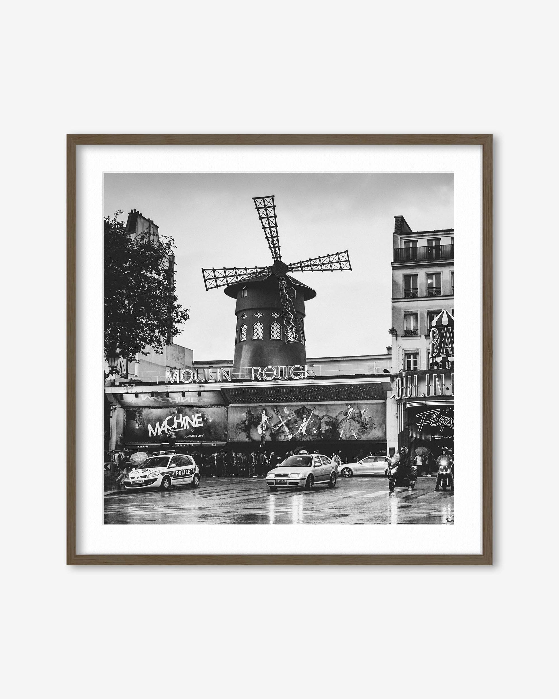 Framed black and white photo of the Moulin Rouge in Paris with cars and people on a rainy day.