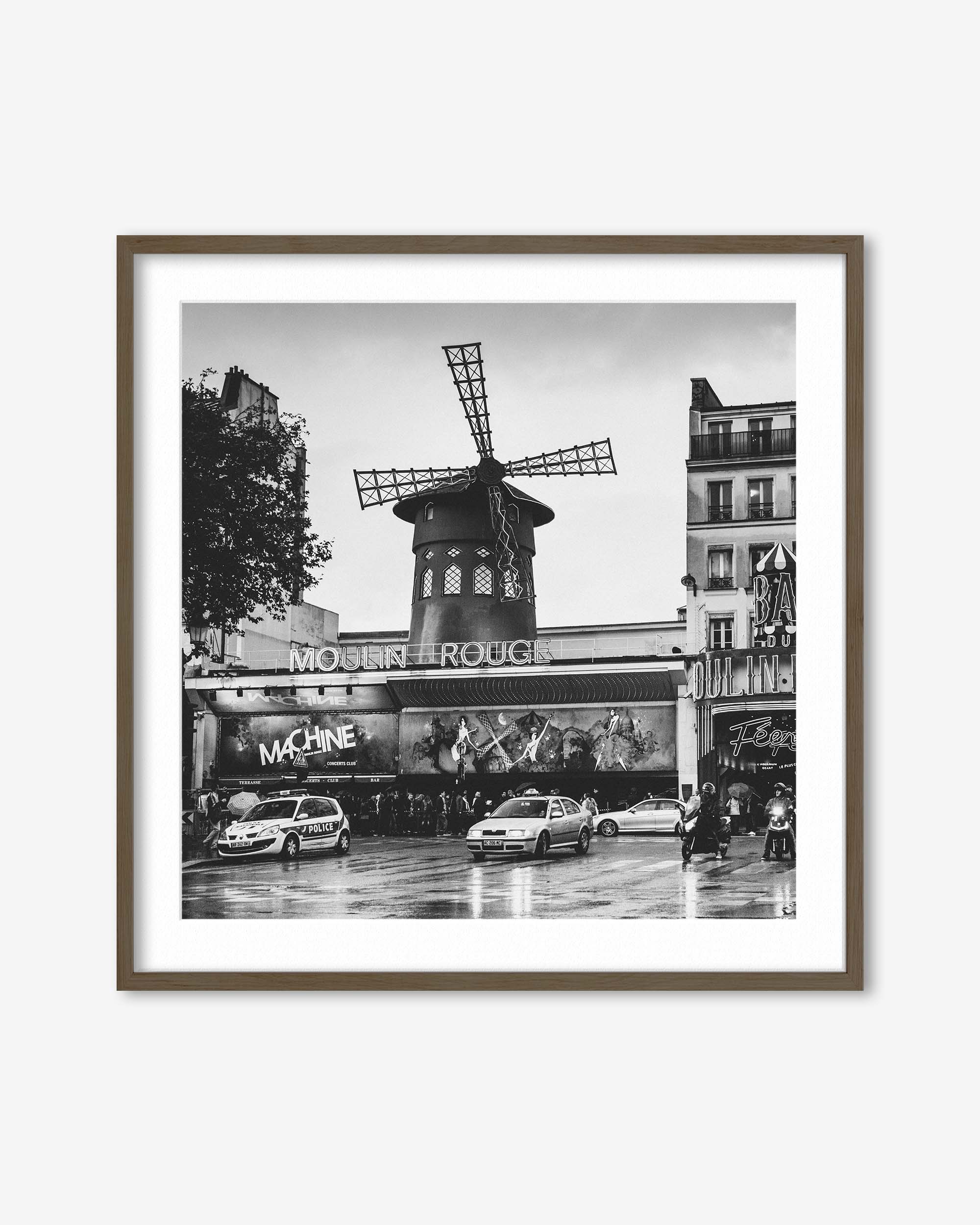 Framed black and white photo of the Moulin Rouge in Paris with cars and people on a rainy day.