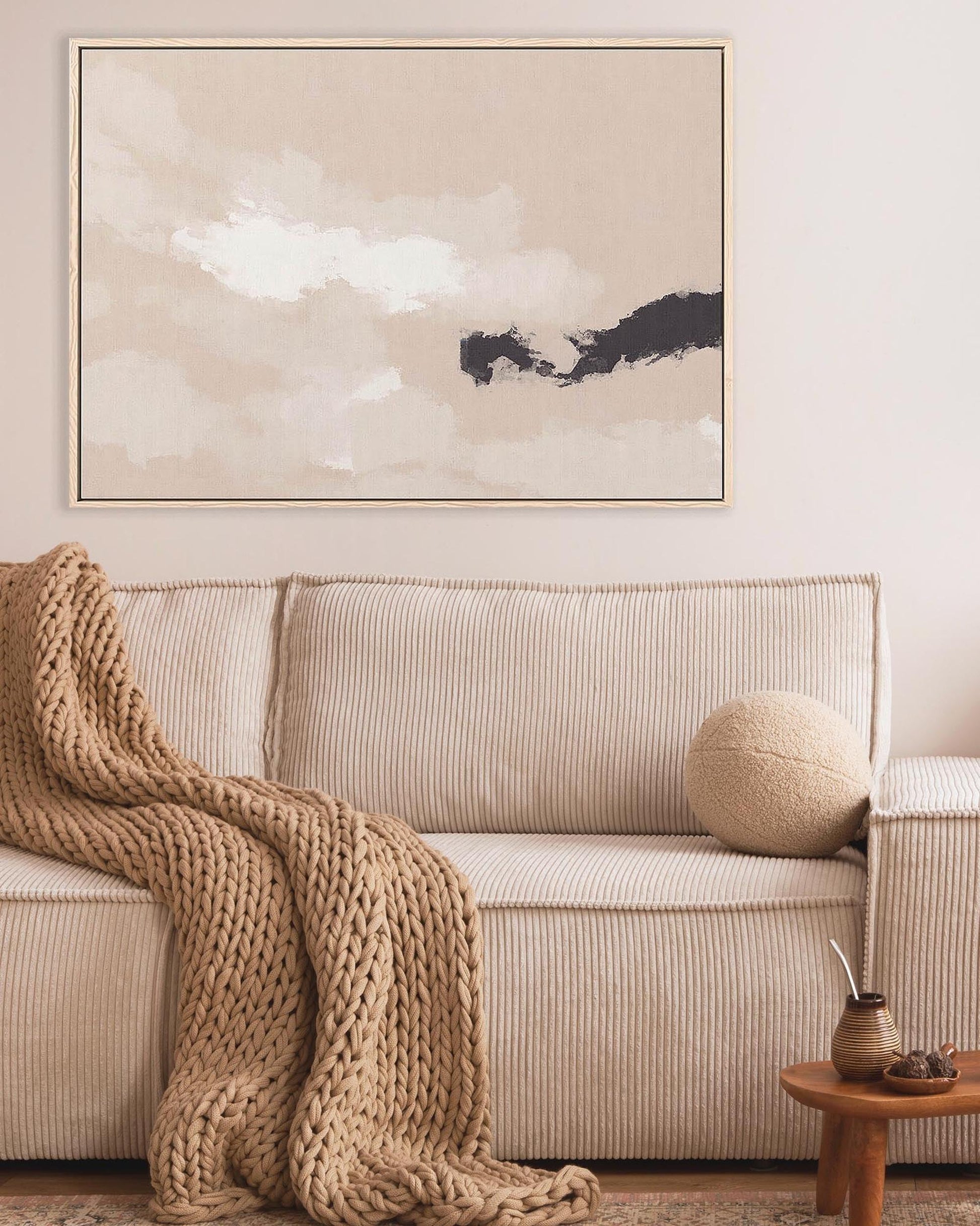 Cozy living room with a beige sofa, chunky knit blanket, and abstract wall art.