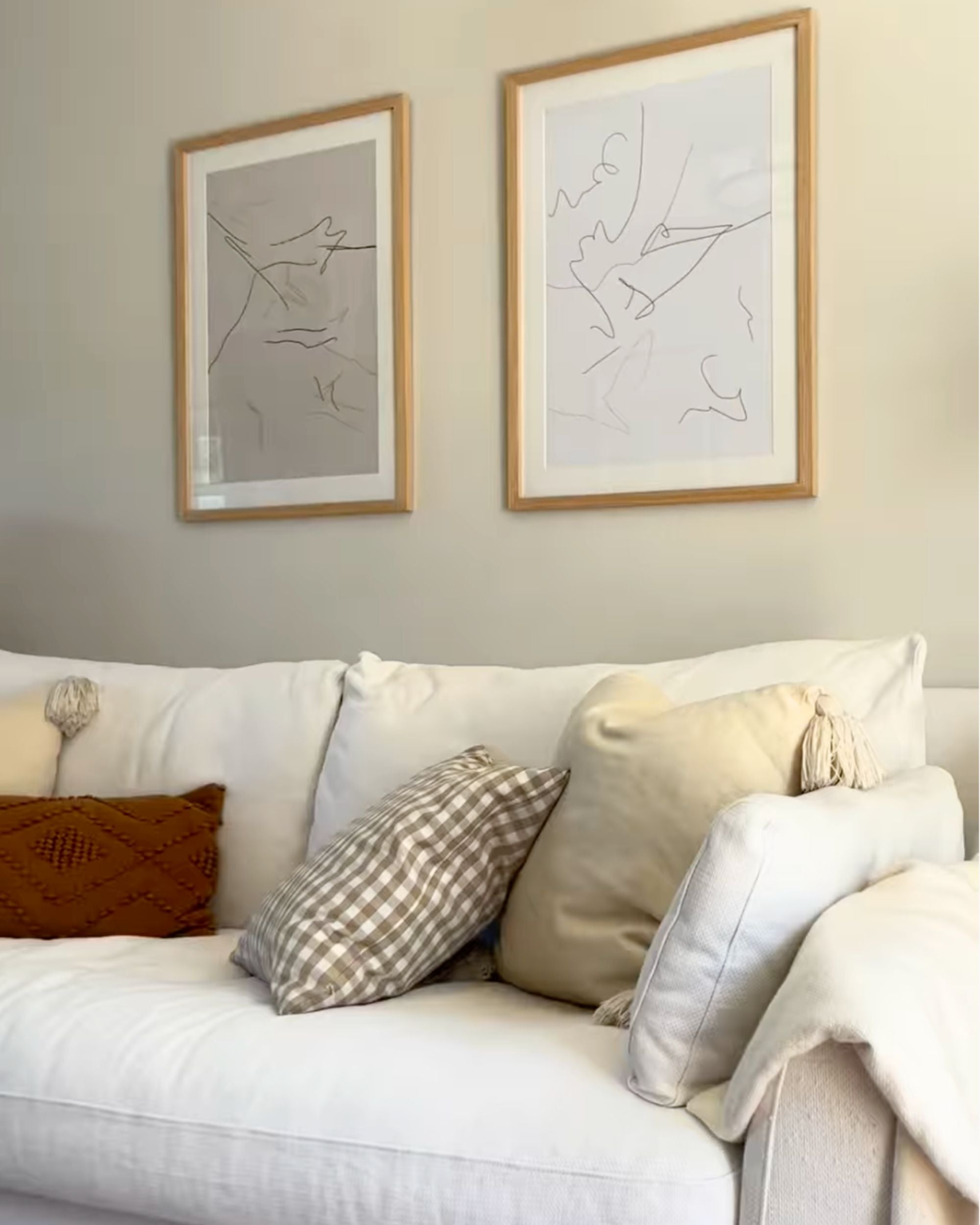 minimal neutral line art prints framed in oak frames in cosy country cottage living room aesthetic with rusty brown cushion and checkered pattern scatter cushion on white linen sofa.