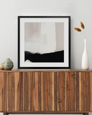 Framed abstract art piece on a wooden sideboard with decorative items.
