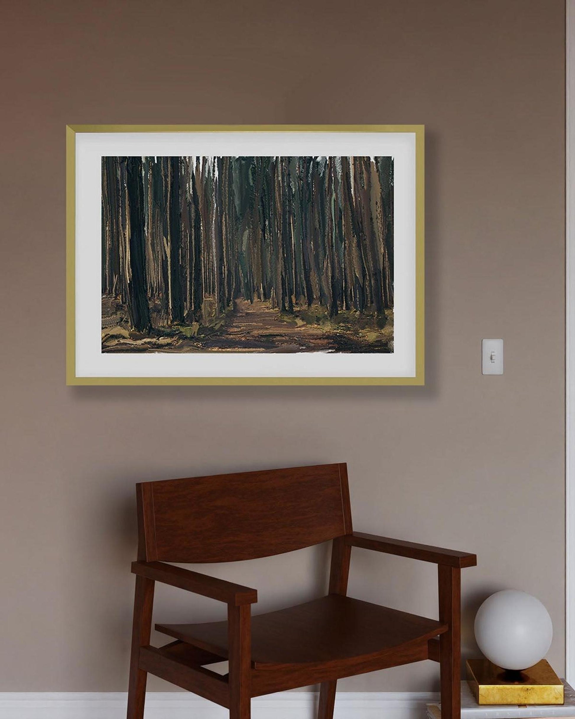 Framed artwork of a forest scene on a wall above a wooden chair.