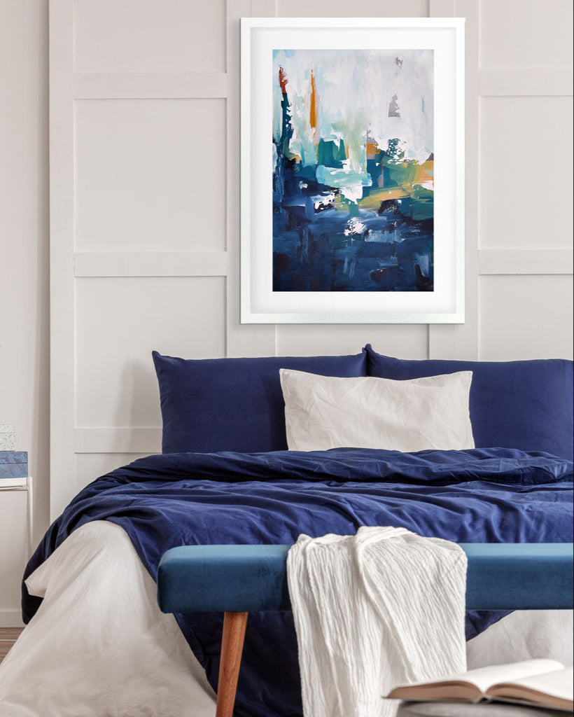 Abstract art print on a wall above a bed with blue bedding.