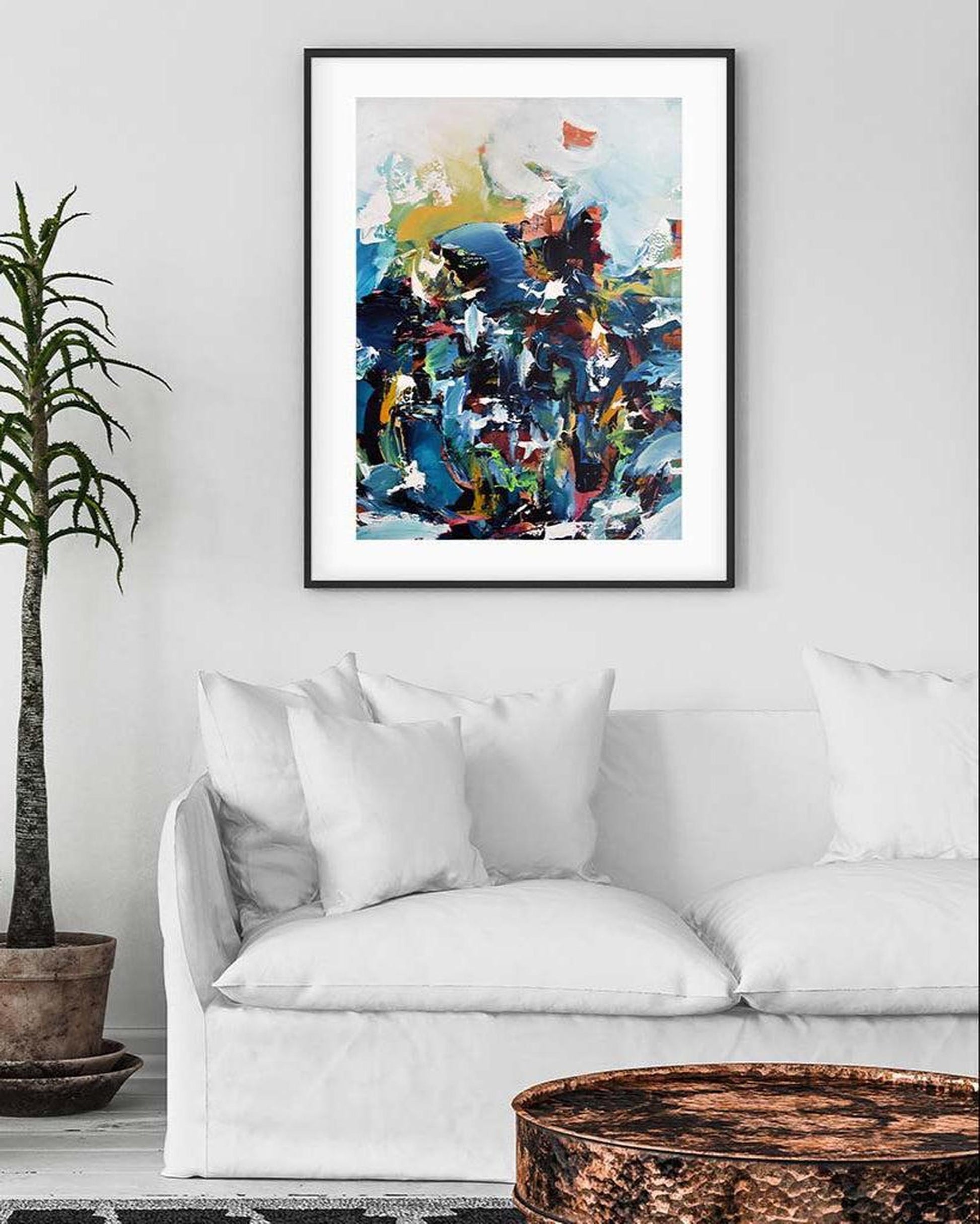 Abstract art print on a wall above a white sofa with decorative pillows.