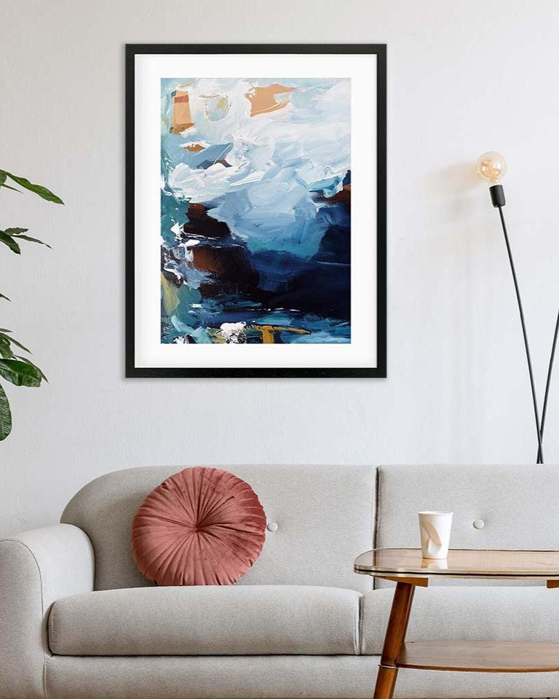 Framed abstract painting on a wall above a sofa with a pink pillow.