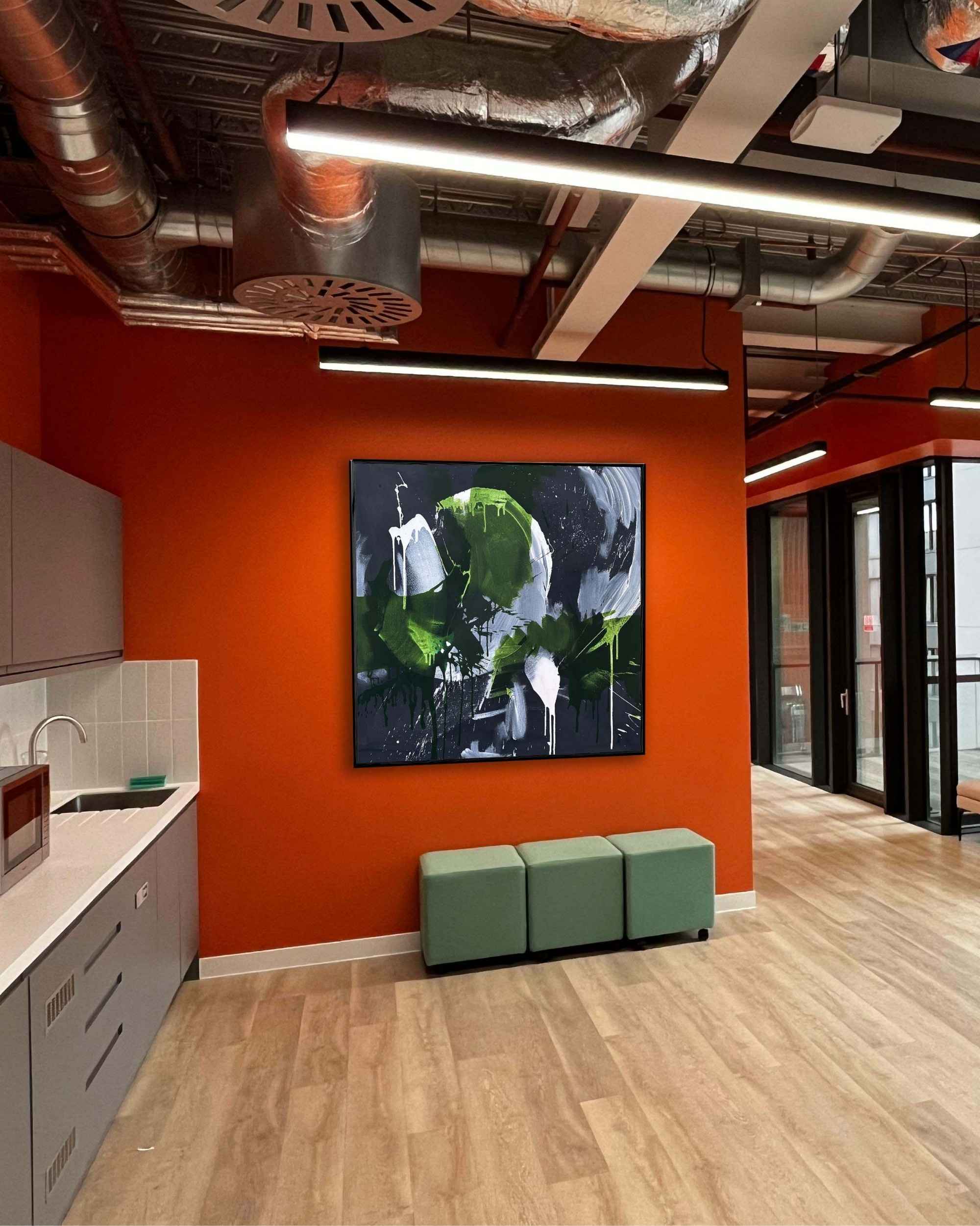 Modern office interior with high end finishes, orange wall, large original artwork, and wooden floor.