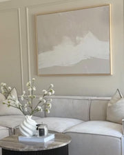 A large beige neutral wall art above a modern sofa in a styled living room