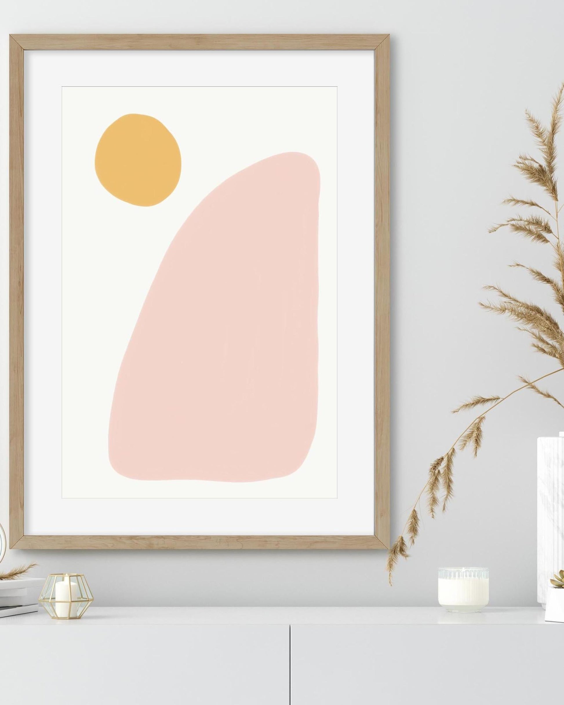 Framed abstract art print with a yellow circle and pink oval on a white wall.