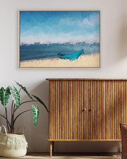 Framed artwork of a blue boat on a beach above a wooden cabinet with a plant and basket below.