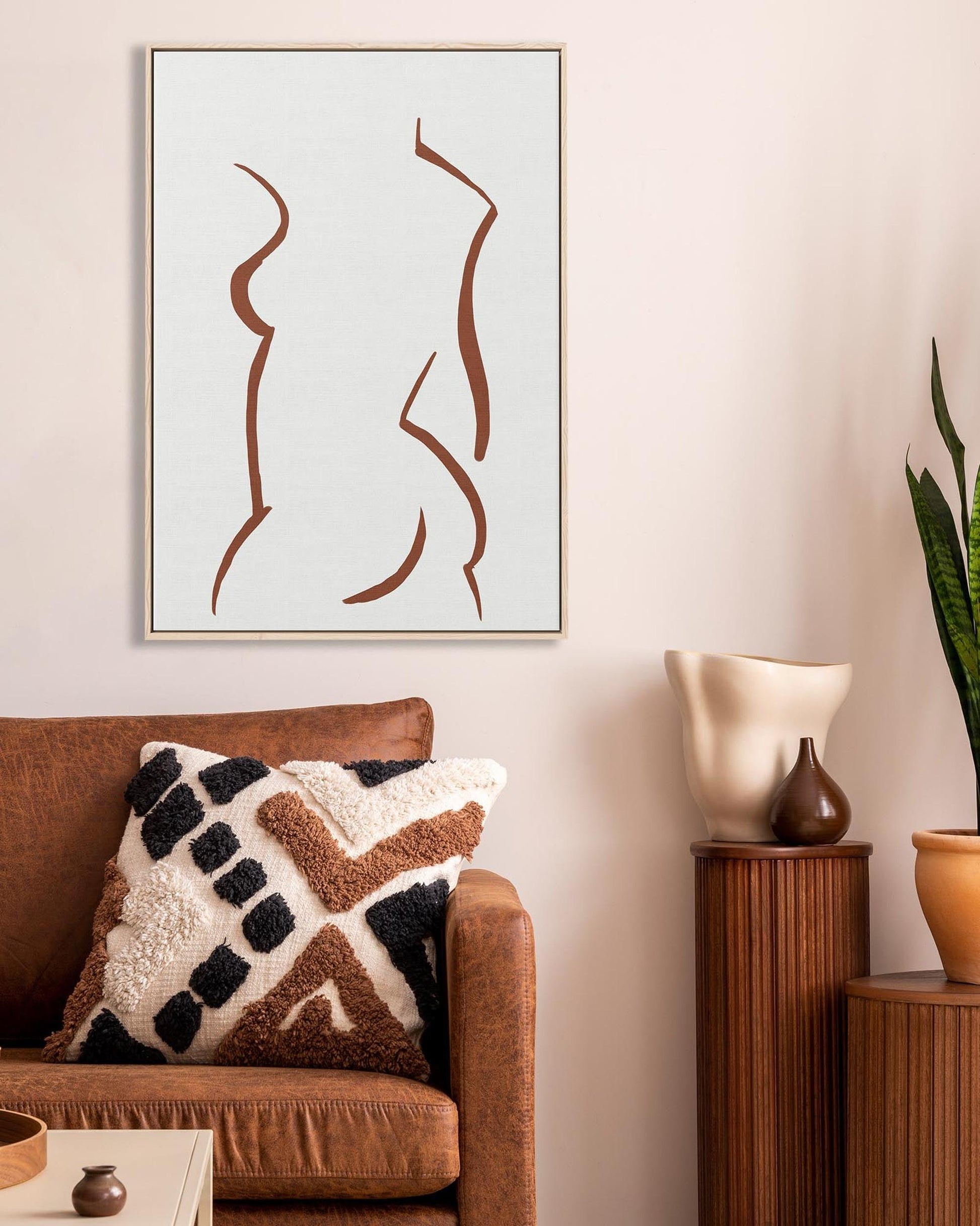 Living room with brown sofa, decorative pillows, abstract art, and a potted plant.
