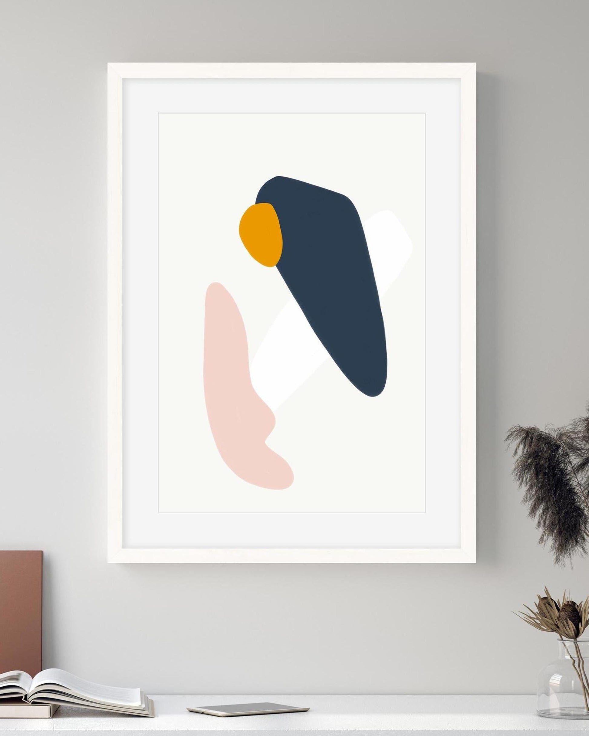 Framed abstract art print with colorful shapes on a gray wall.