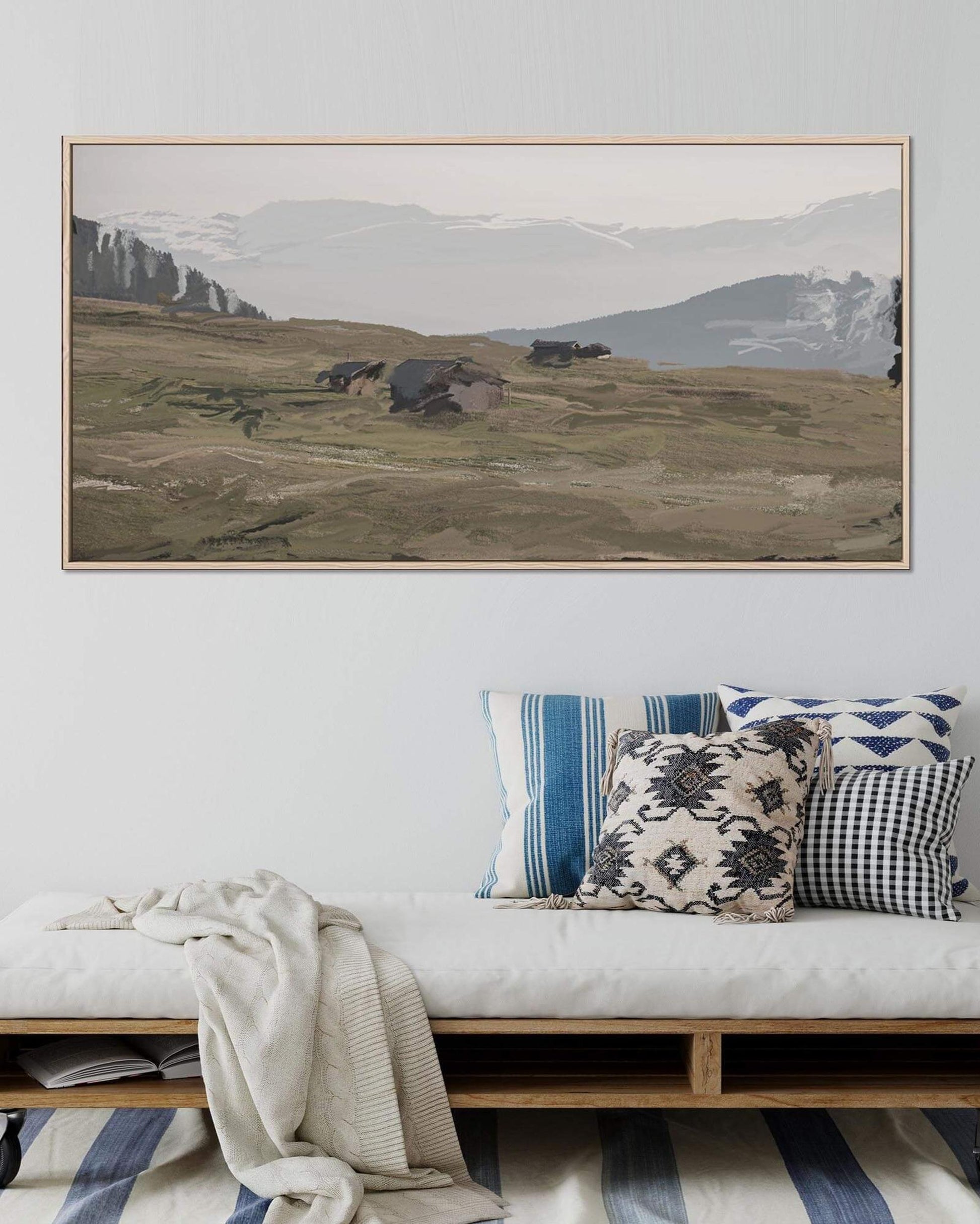 Framed landscape painting above a bench with decorative pillows in a living room setting.