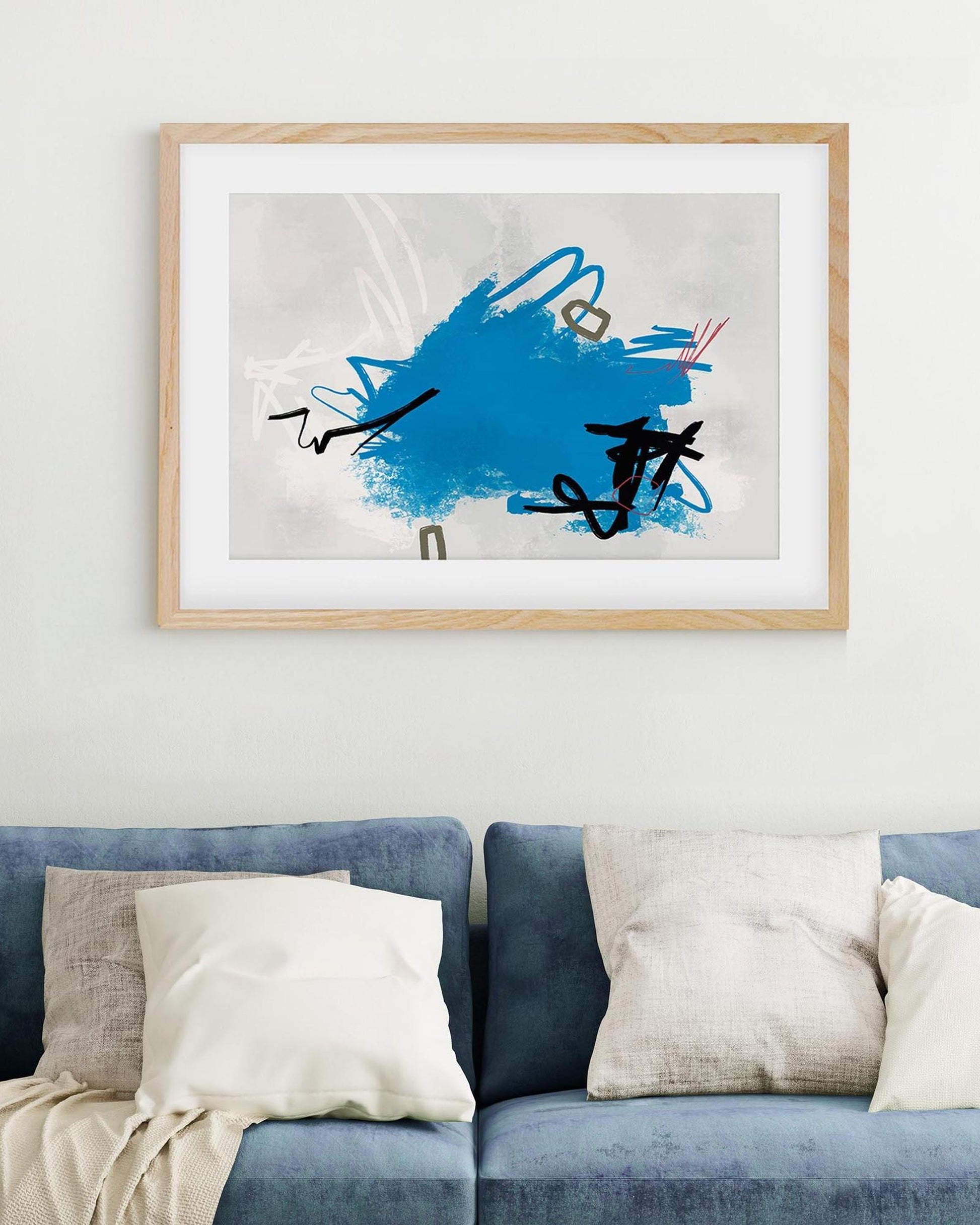 Abstract art print with blue and black design in a wooden frame above a sofa.