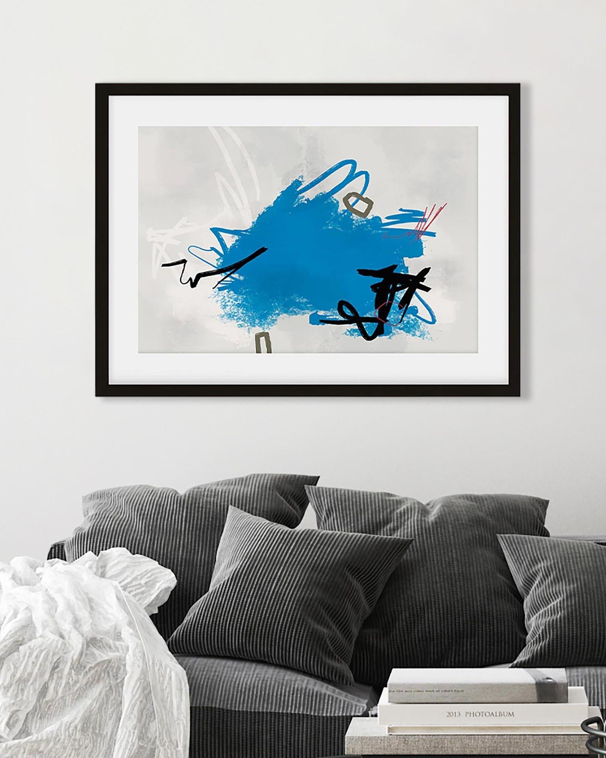 Framed abstract art piece with blue and black design on a white wall above a gray sofa.