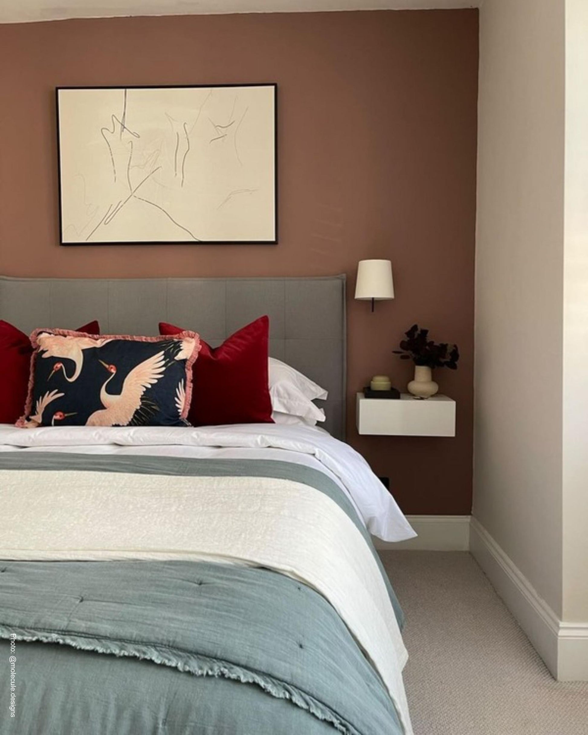 Bedroom with a bed featuring colorful pillows, a nightstand with a lamp, and abstract art on the wall.