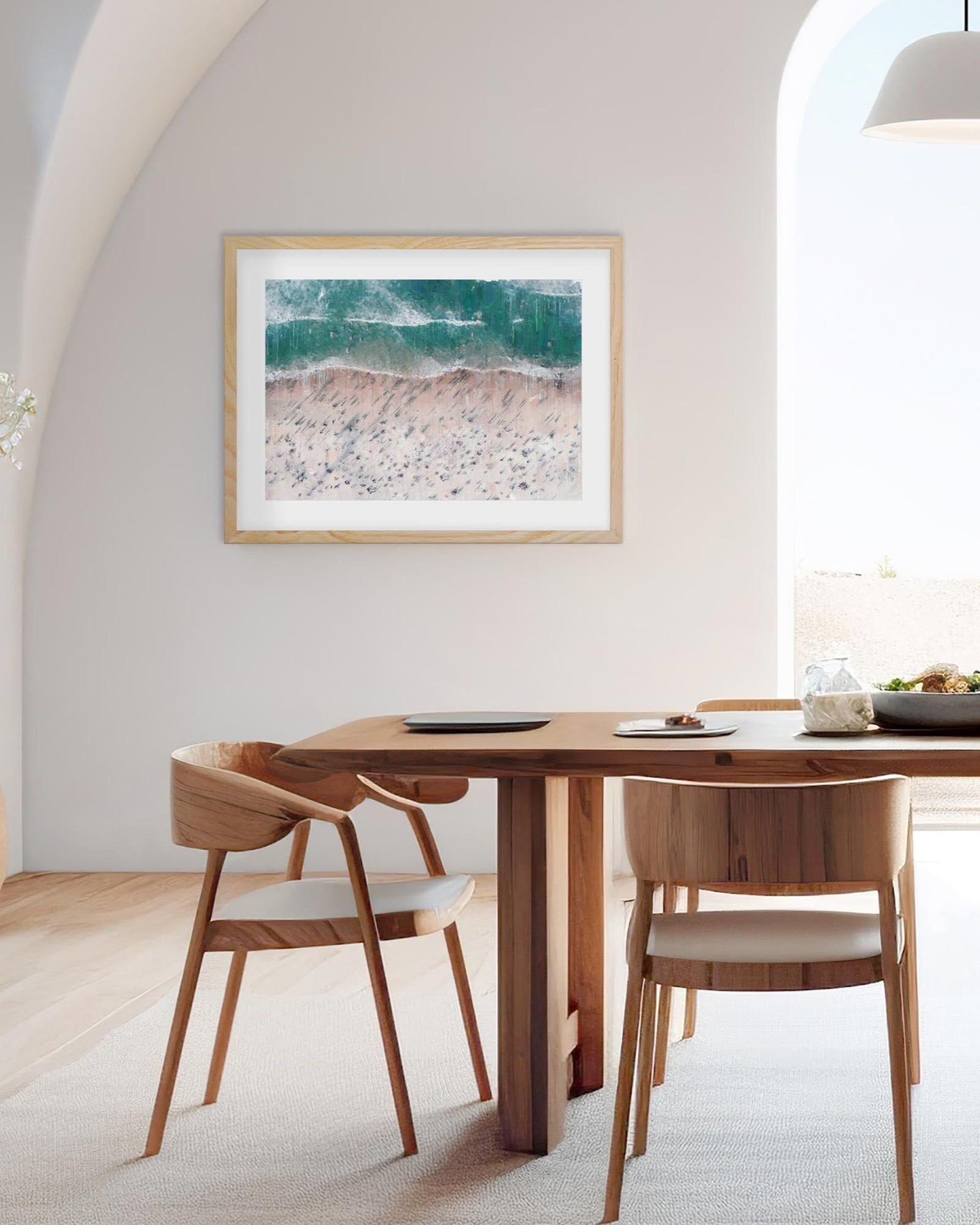 Dining room with wooden table and chairs, framed beach scene artwork on wall.