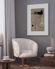 A framed art print depicting a stylized, abstracted representation of a figure in brown tones, displayed on a wall above a modern armchair in a well-lit room.