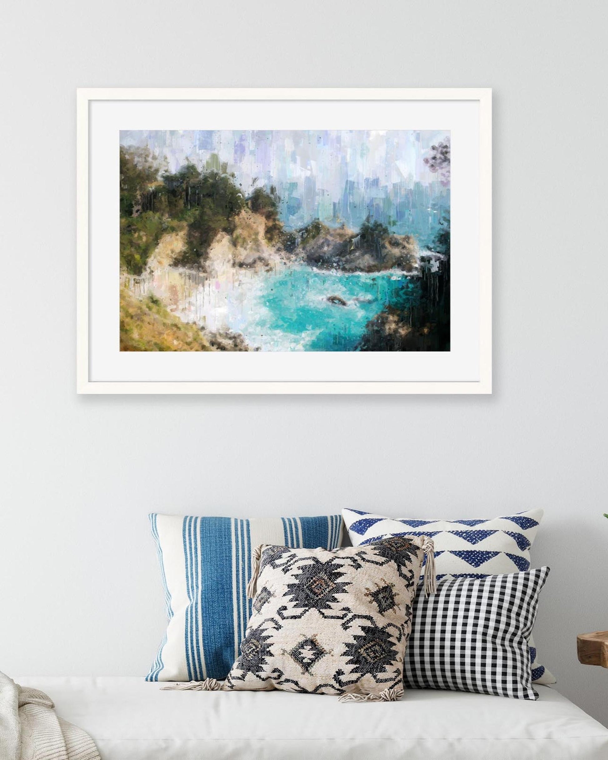 Framed artwork of a coastal scene above a sofa with patterned cushions.