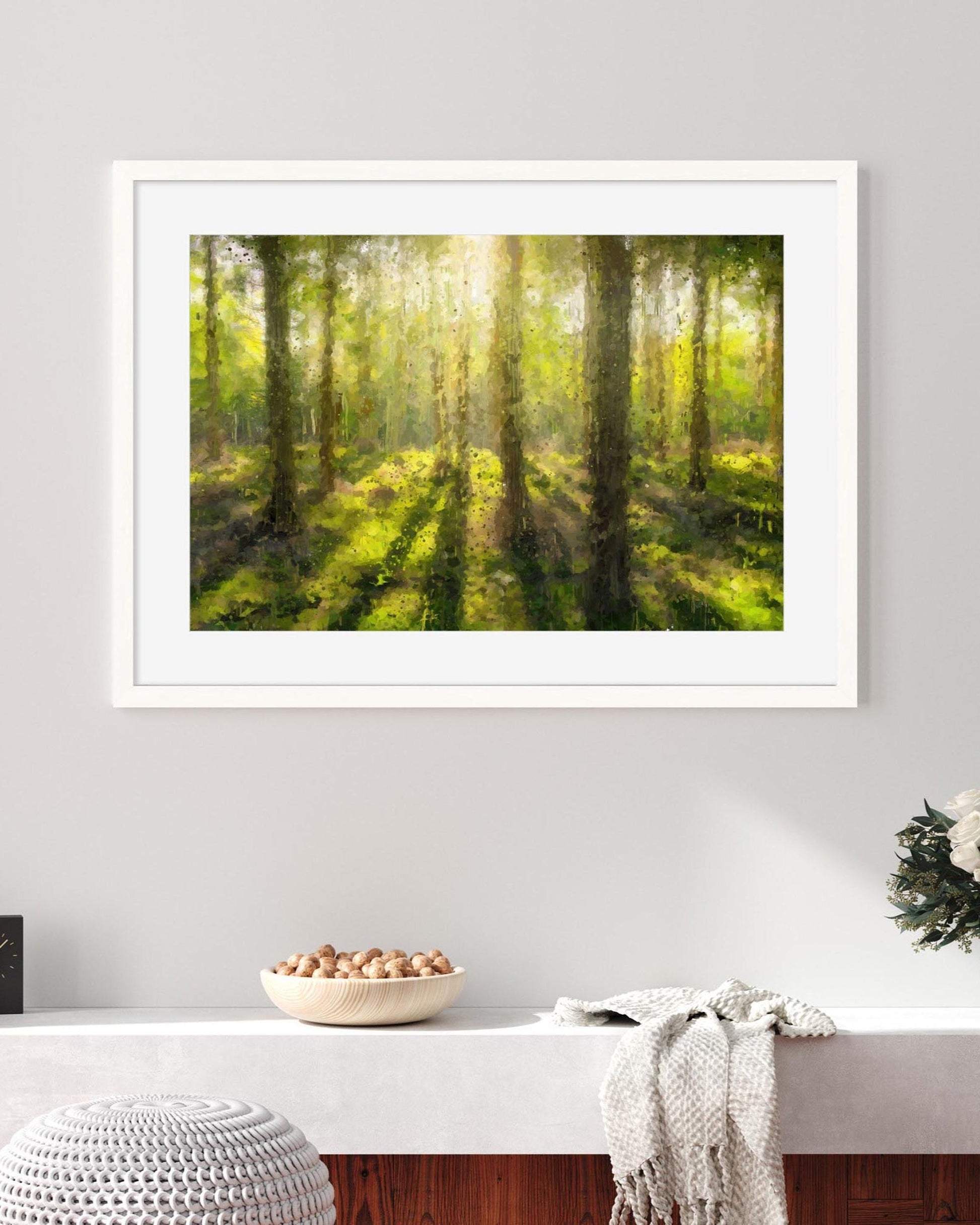 Framed print of a forest scene on a wall above a white shelf with decorative items.