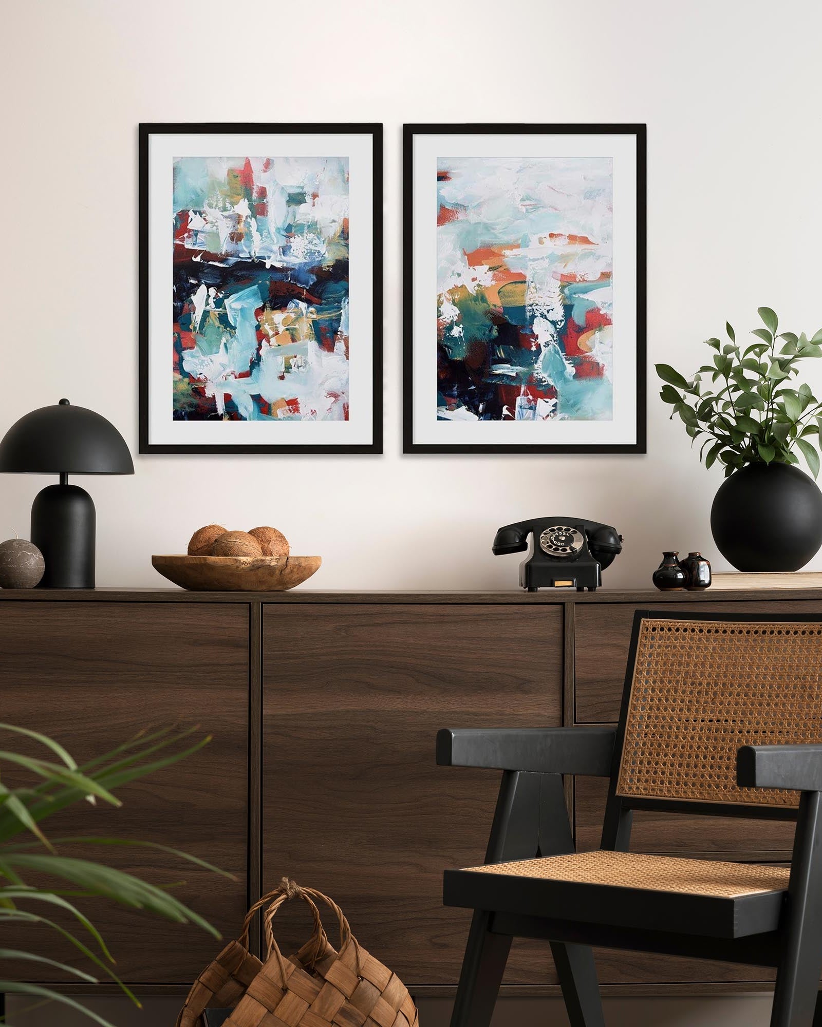 A pair of abstract art prints with turquoise and white colors, displayed on a wall above a wooden console table, with a black chair and decorative items in the setting.