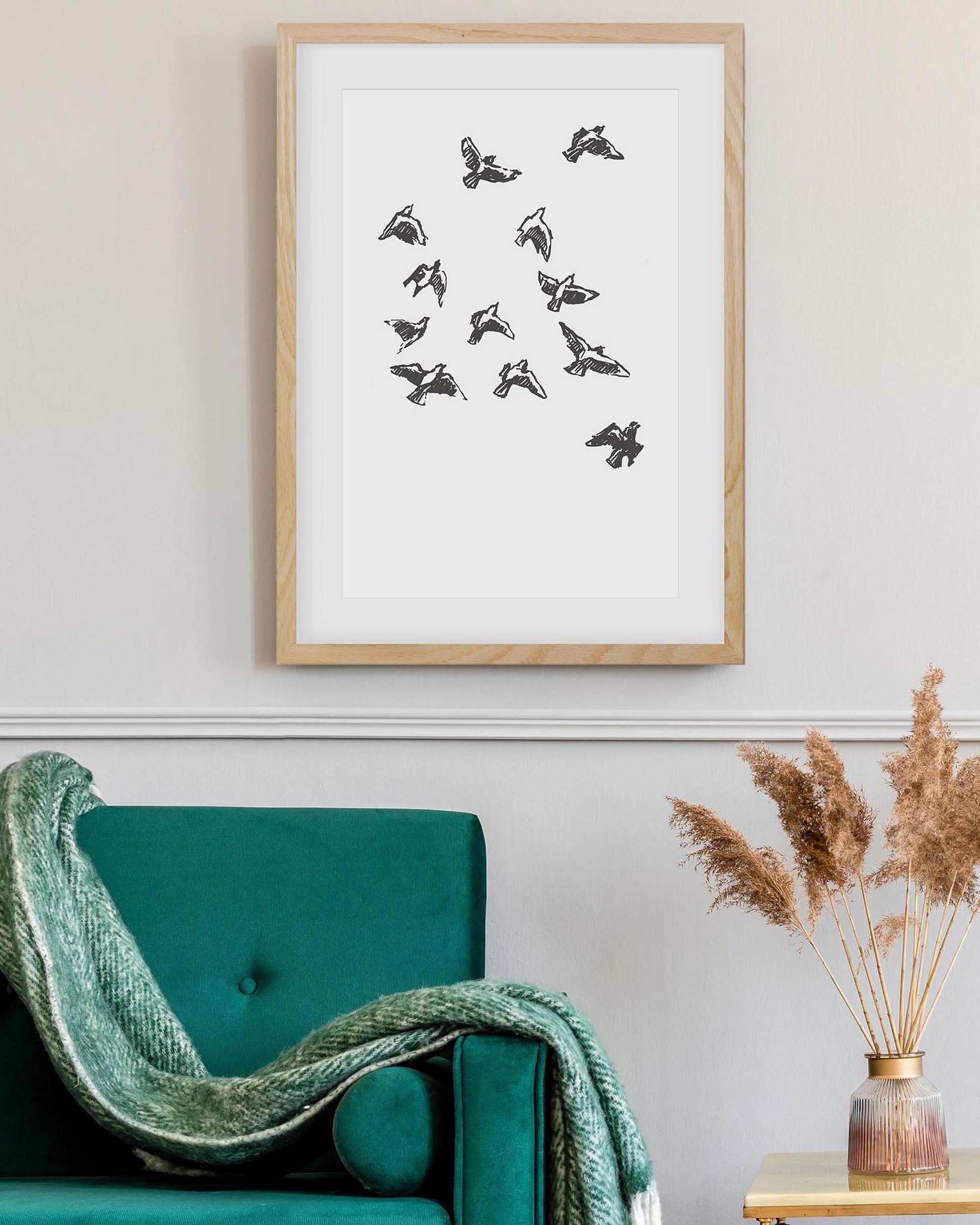 Framed artwork of birds on a white background above a teal sofa with a green blanket.