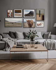 Living room with a gray sofa, wooden coffee table, and wall art displaying landscapes and animals.